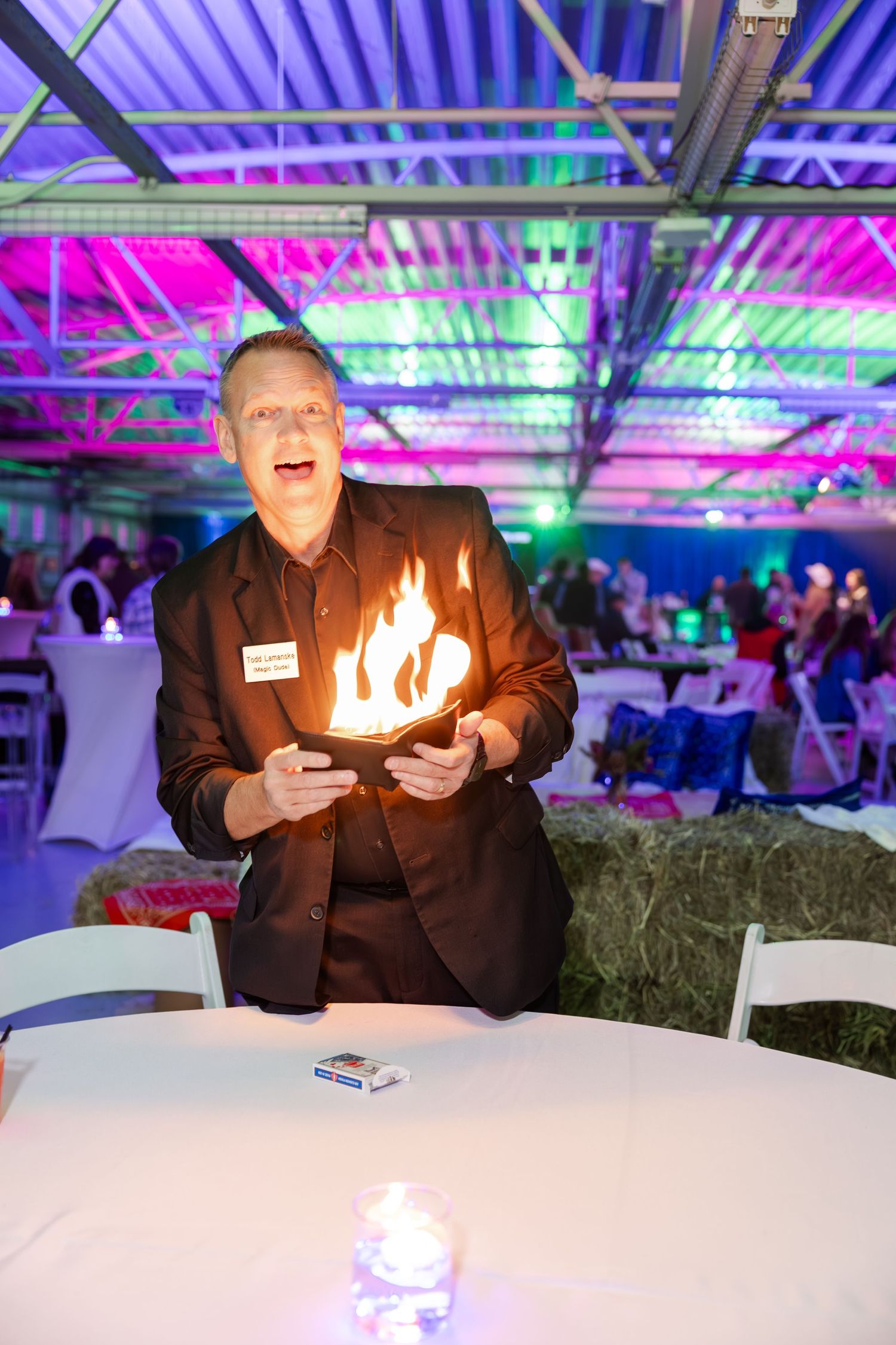Entertainer performs a fire magic trick at a colorfully lit indoor event venue.