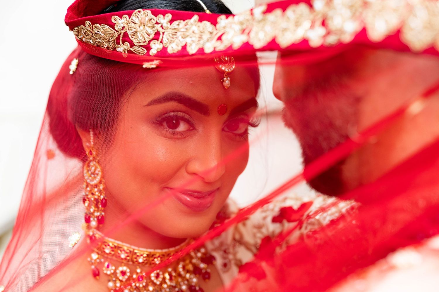 Close-up of Indian bride wearing red bridal veil, gold jewelry, and floral hair accessory.