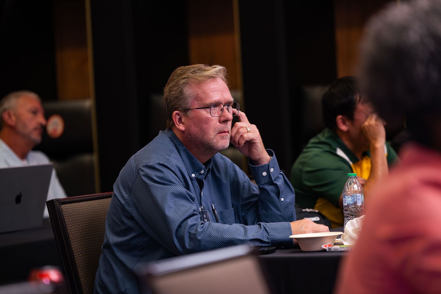 Attentive businessman in blue shirt listening at conference table during professional development seminar.