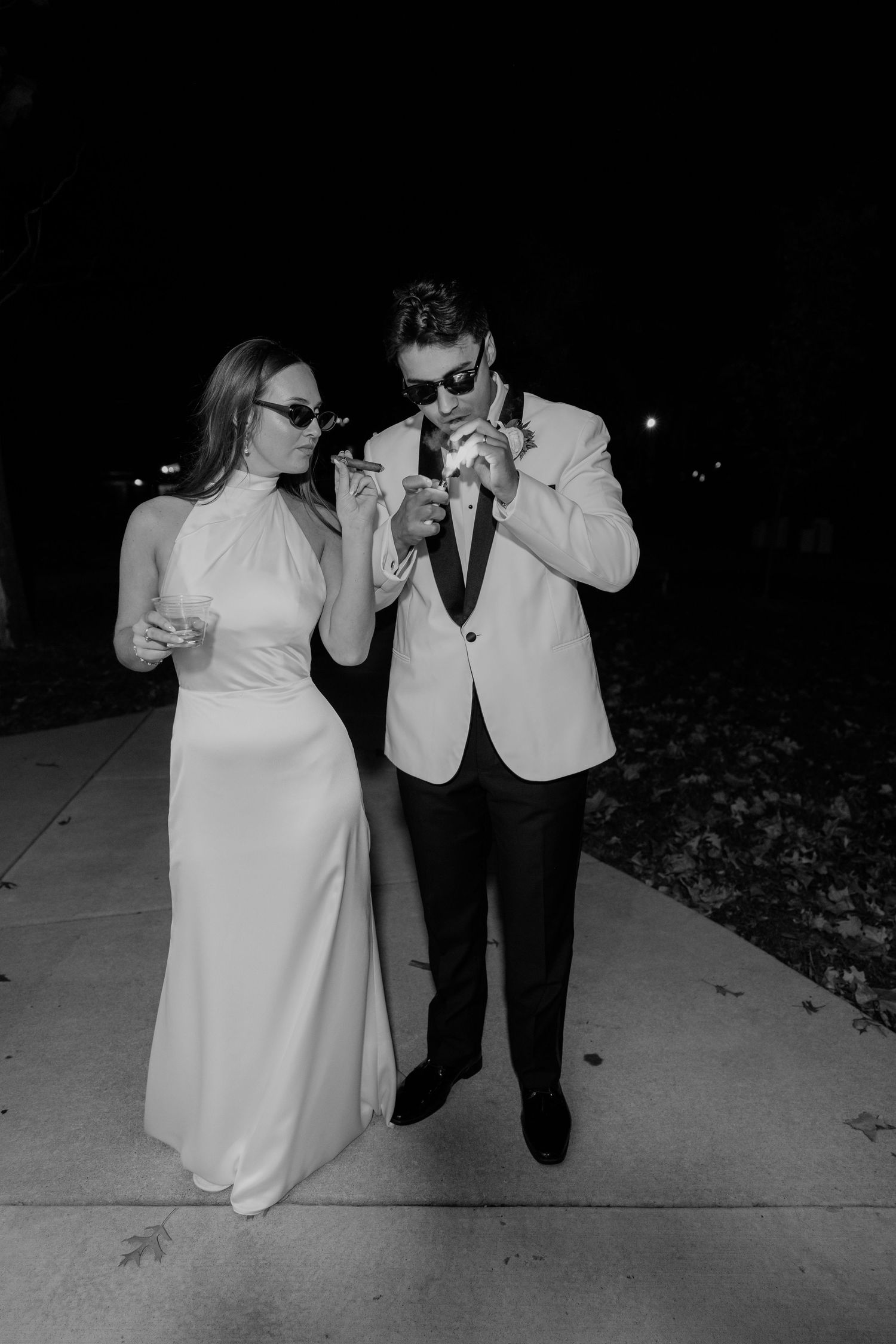 Bride and groom in black and white photo wearing sunglasses outdoors at night after wedding celebration.
