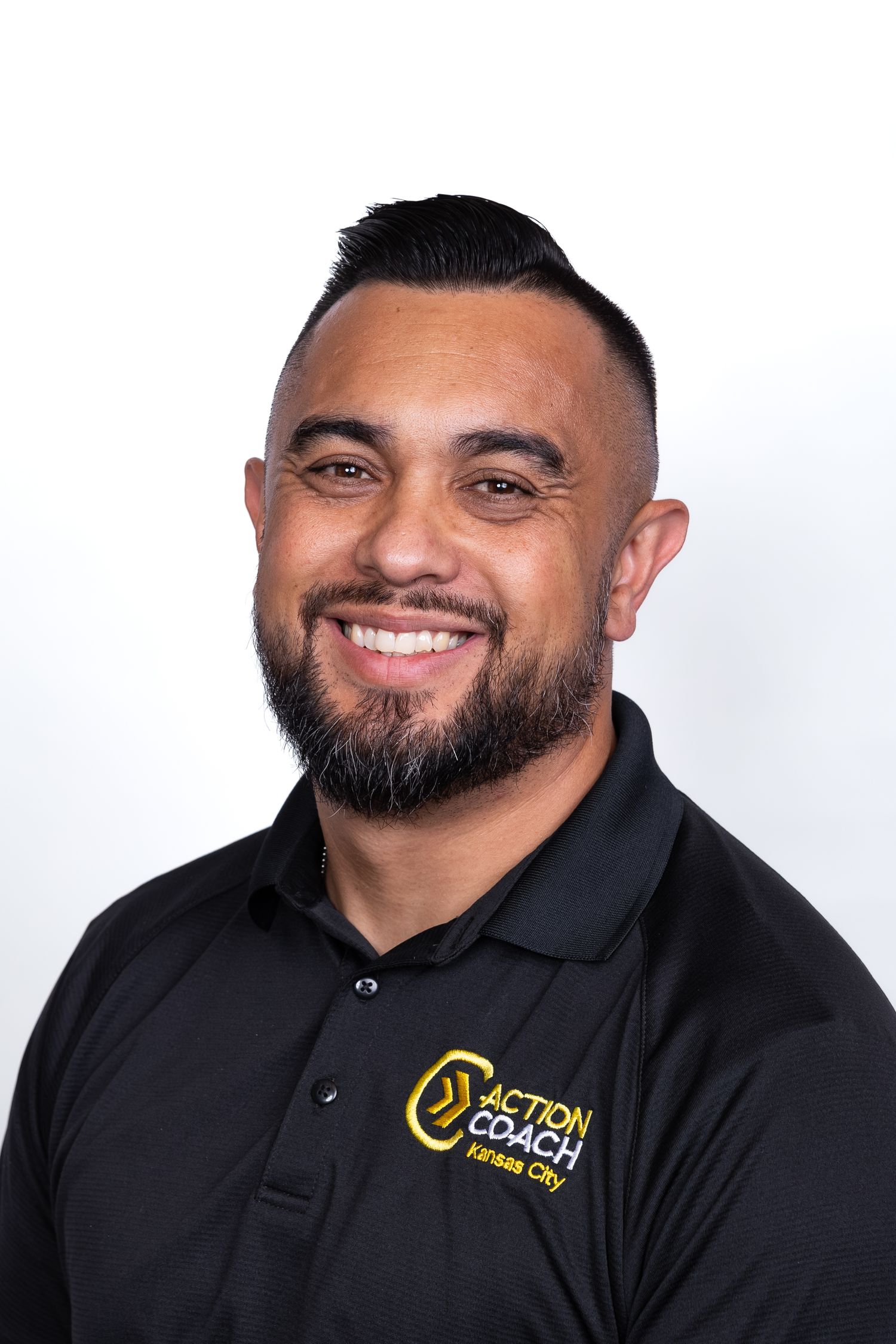 Smiling man with beard wearing black Action Coach Kansas City polo shirt against white background.
