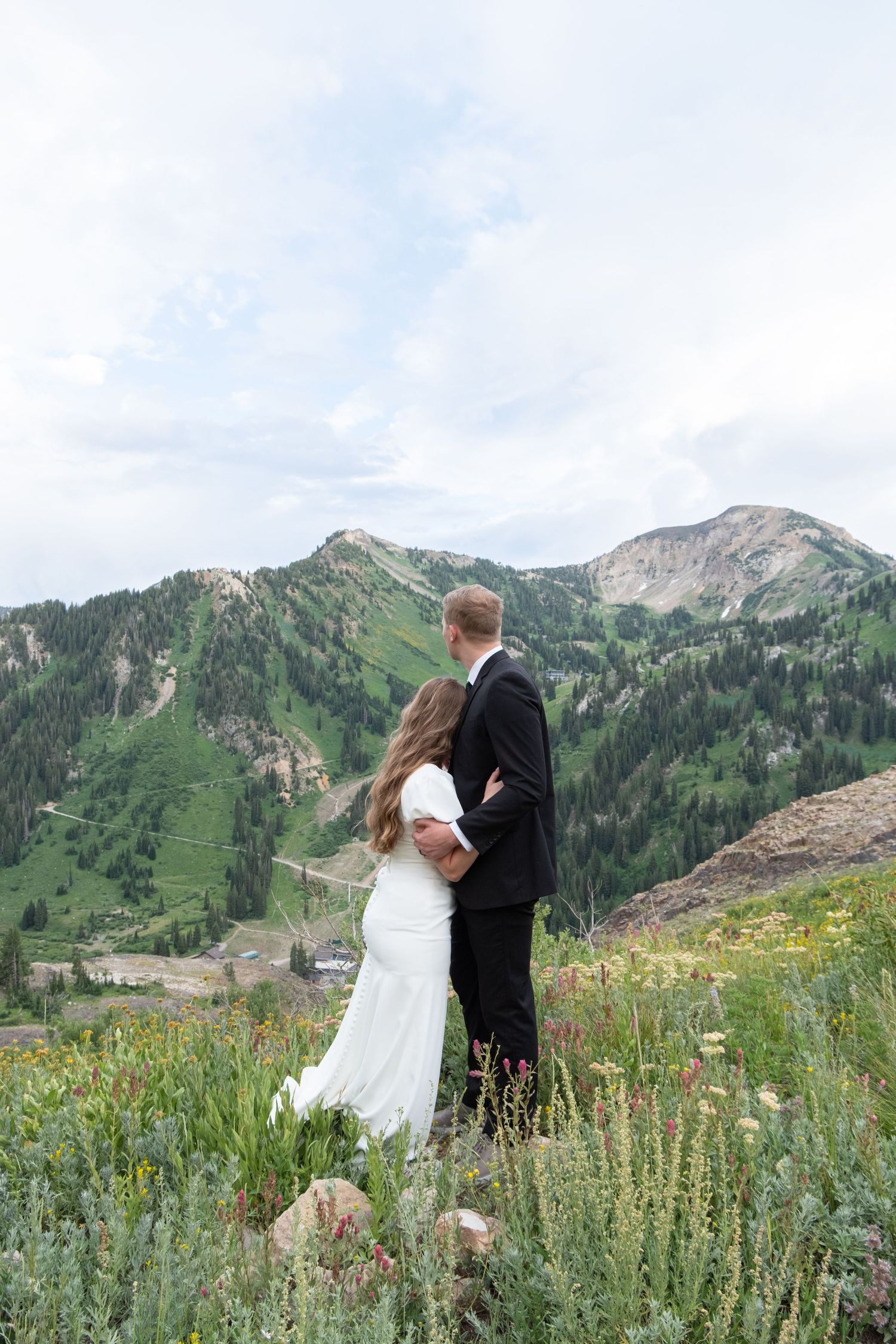 Wedding couple shares an intimate moment in a mountain meadow filled with wildflowers and alpine peaks.
