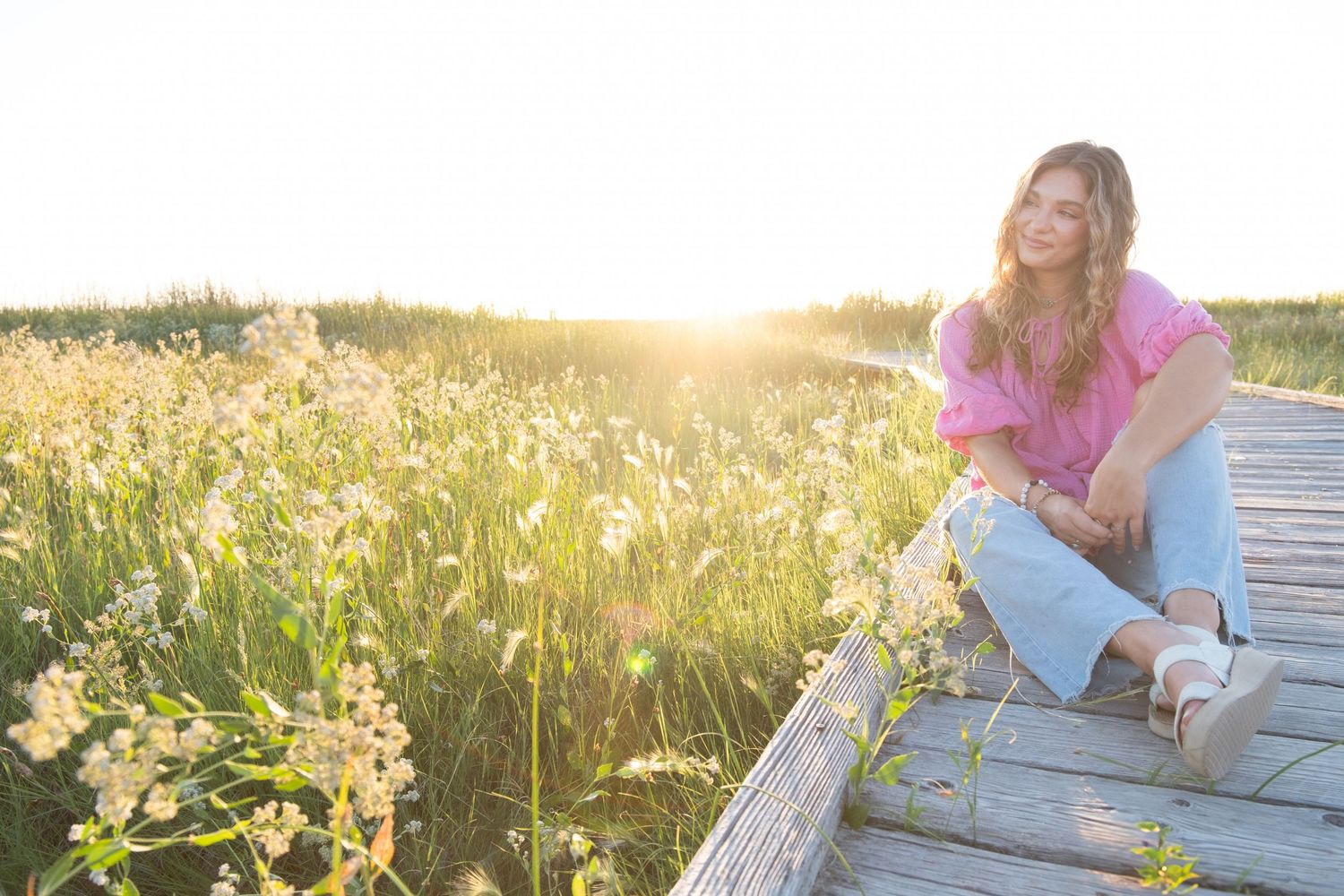 Person sits on wooden stairs beside a sunlit wildflower meadow at golden hour.