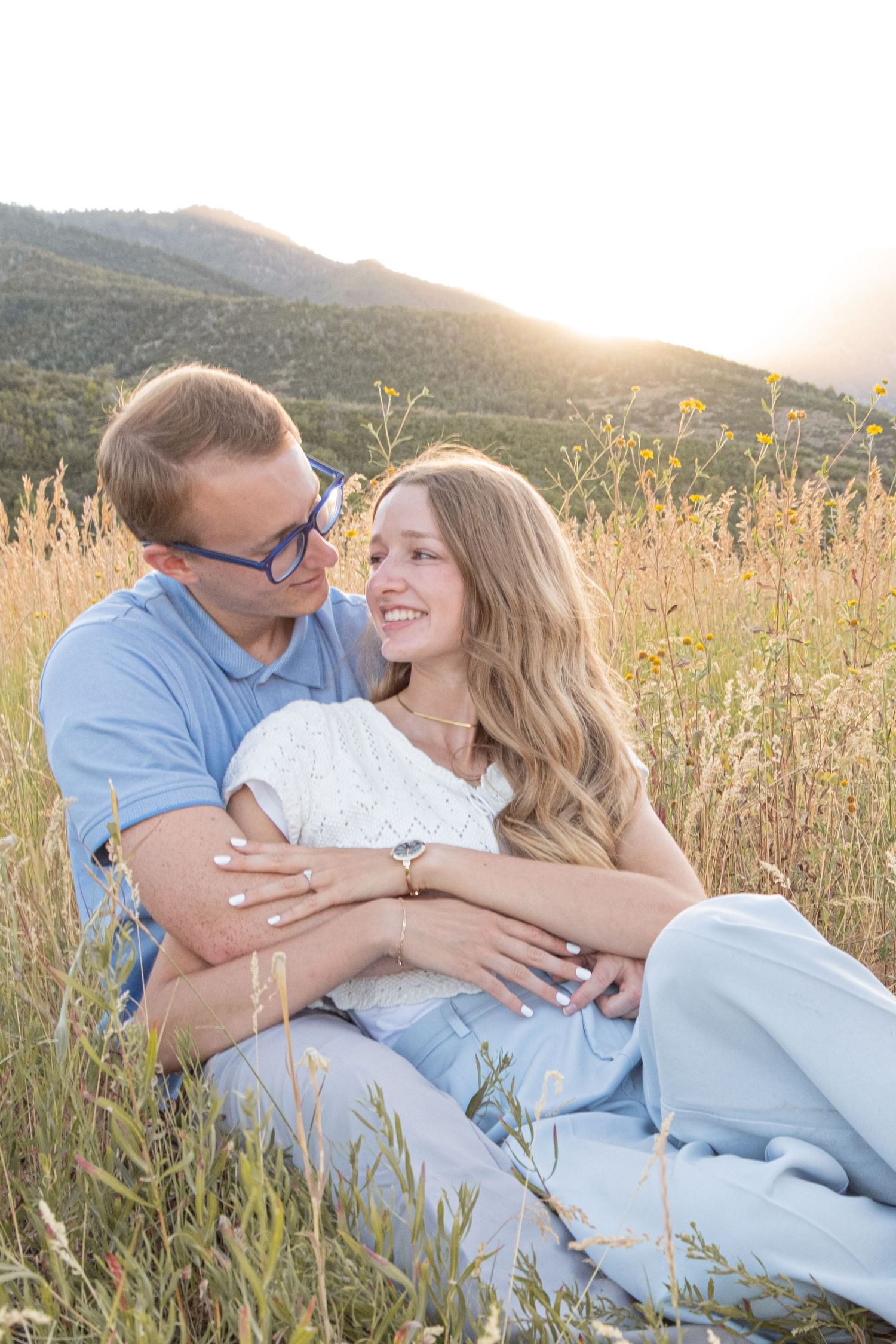 A couple in casual blue outfits share intimate moments while laying in a golden wildflower field at sunset.