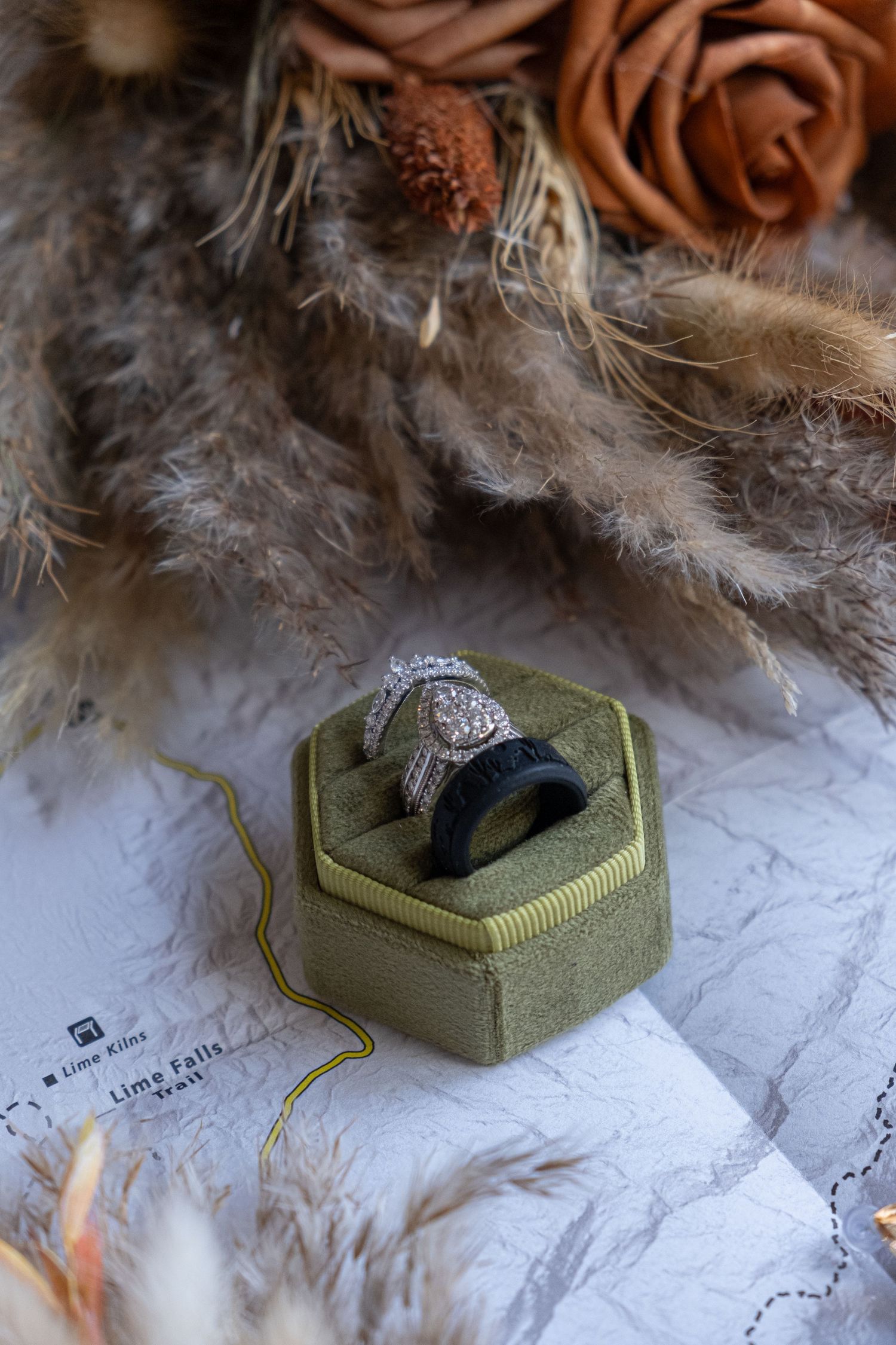 Diamond engagement ring displayed in olive green hexagonal velvet ring box with feathers and floral decorative elements for an elopement.