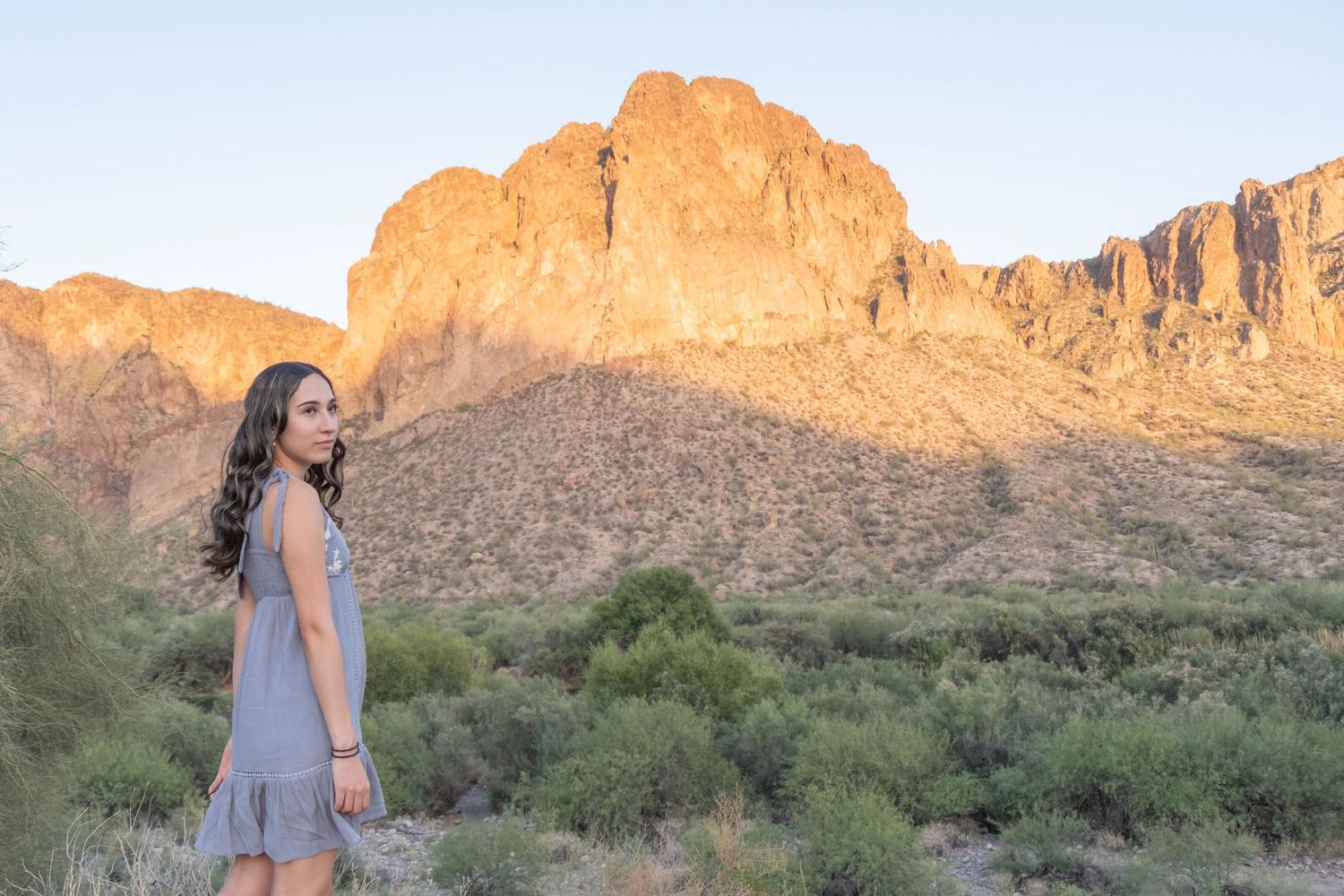 Desert mountains glow orange in evening light as cacti dot the landscape during a portrait session.