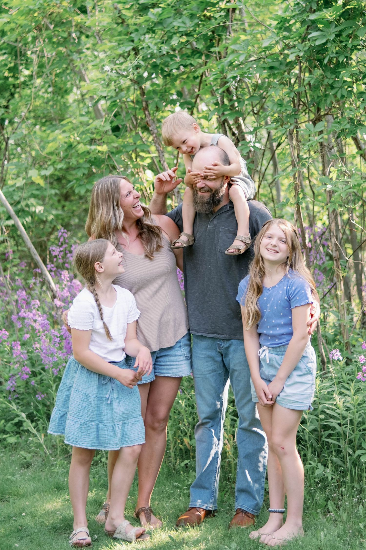 Candid family moment in a forest setting with wildflowers.