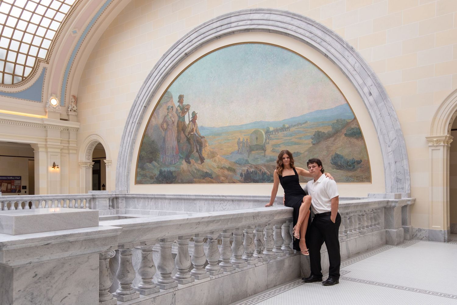 Couple posing in front of a large landscape mural on a marble balcony inside an elegant historic building.