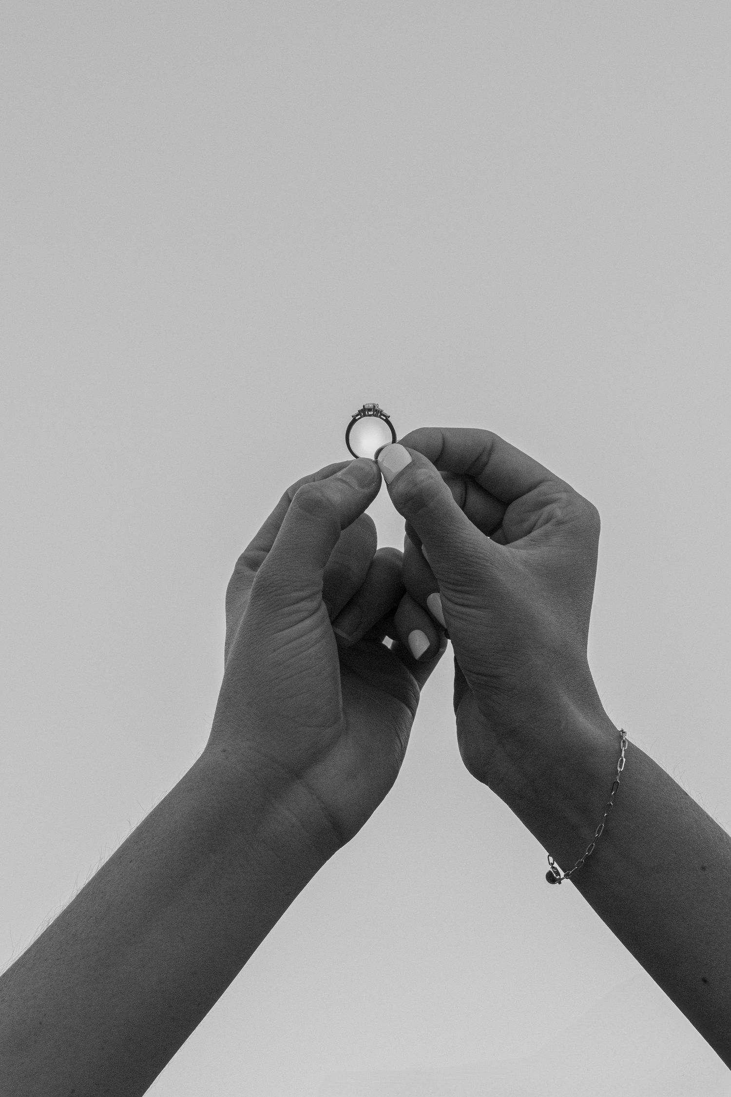 Black and white close-up of hands holding an engagement ring against a plain background.