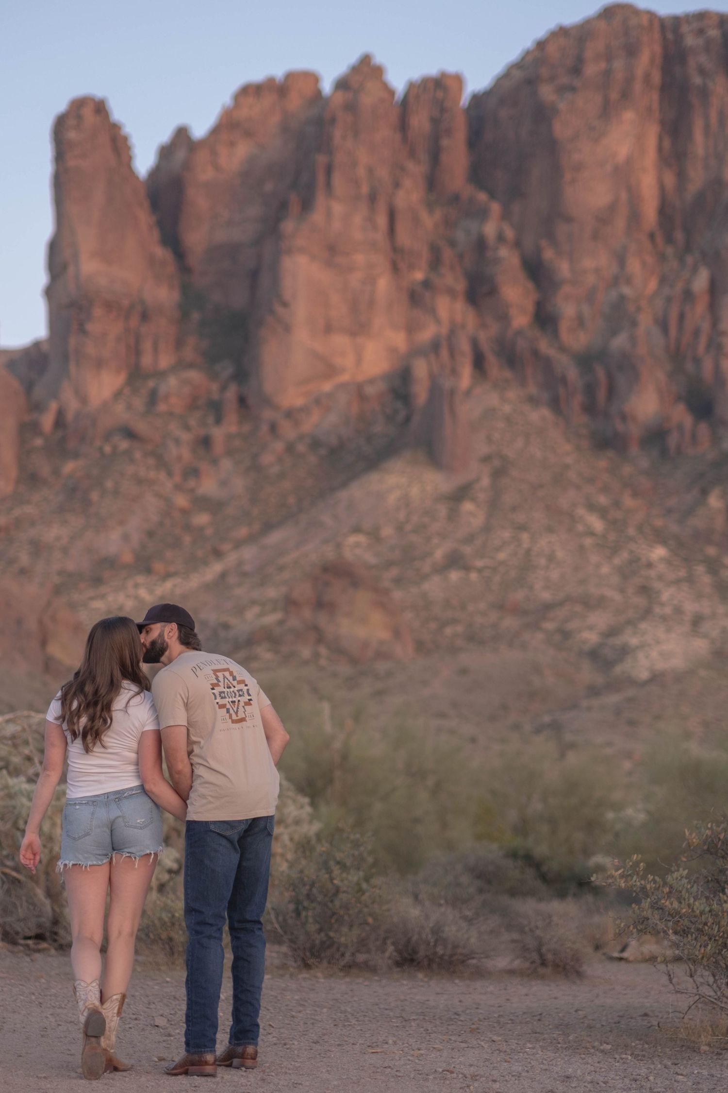 A couple walks together on a desert trail with the Superstition Mountains looming in the background.