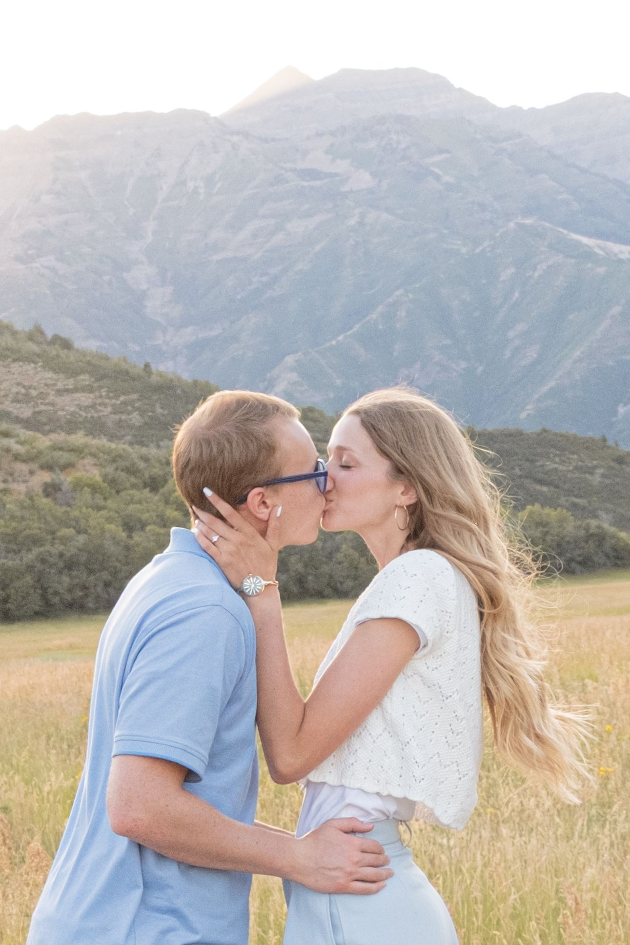 A couple share an intimate moment in a golden meadow with majestic mountains in the background at sunset.