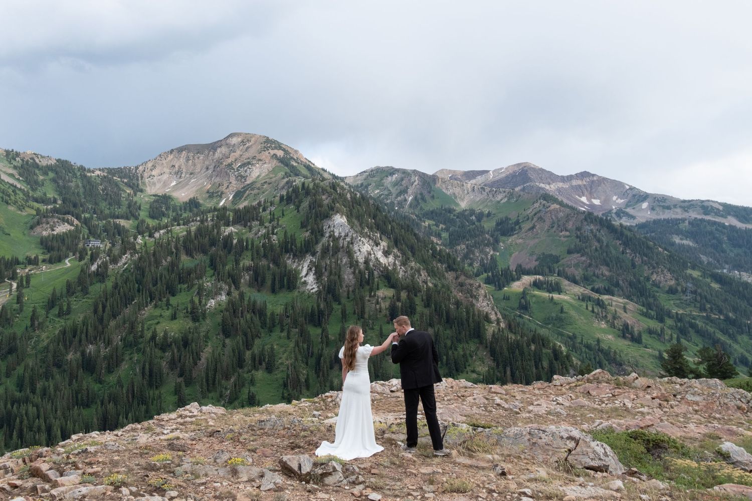 Mountain wedding couple shares romantic moment on scenic alpine meadow with wildflowers and dramatic peaks.