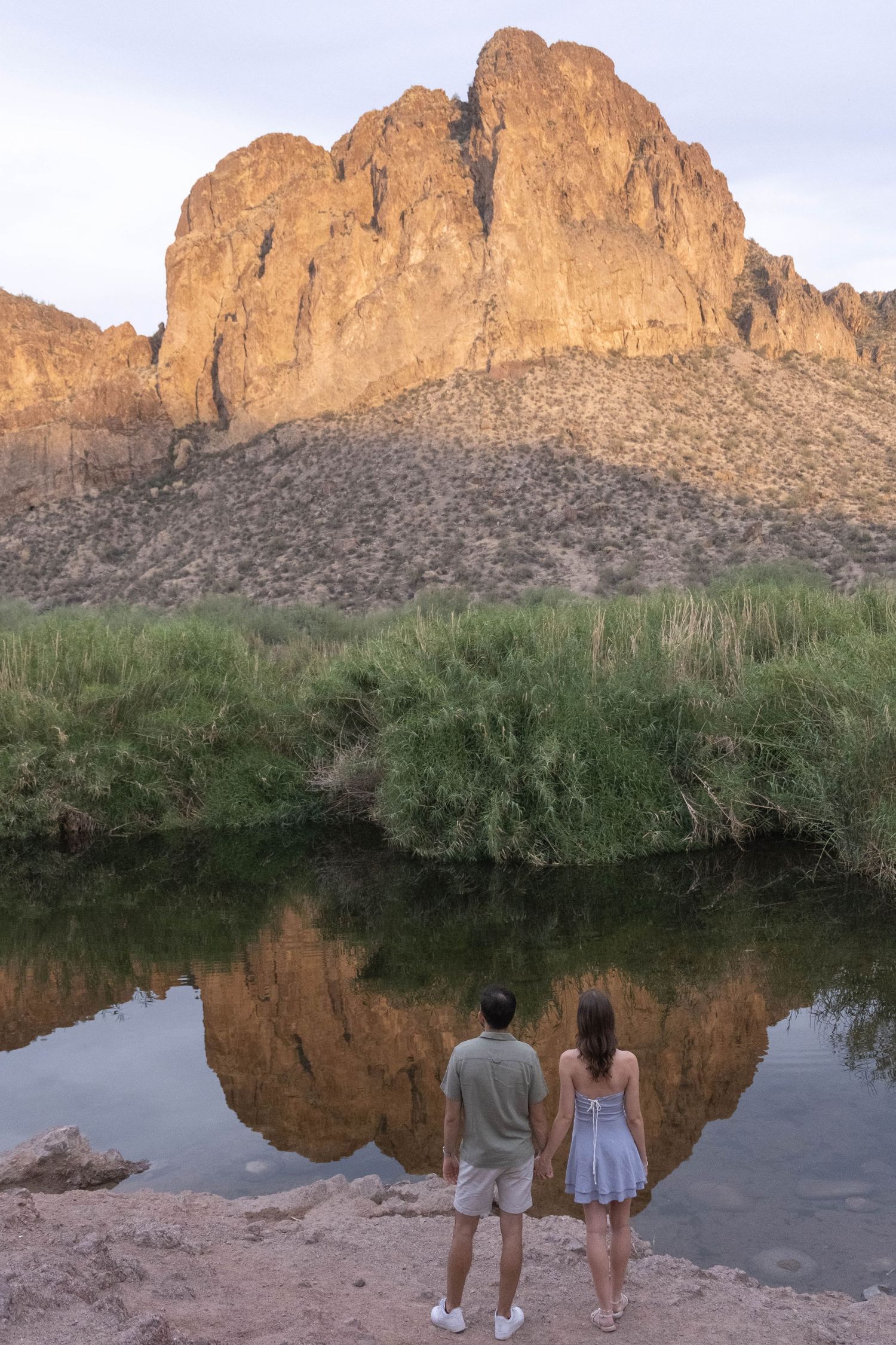 A couple stands silhouetted against a dramatic mountain reflection in a still lake.