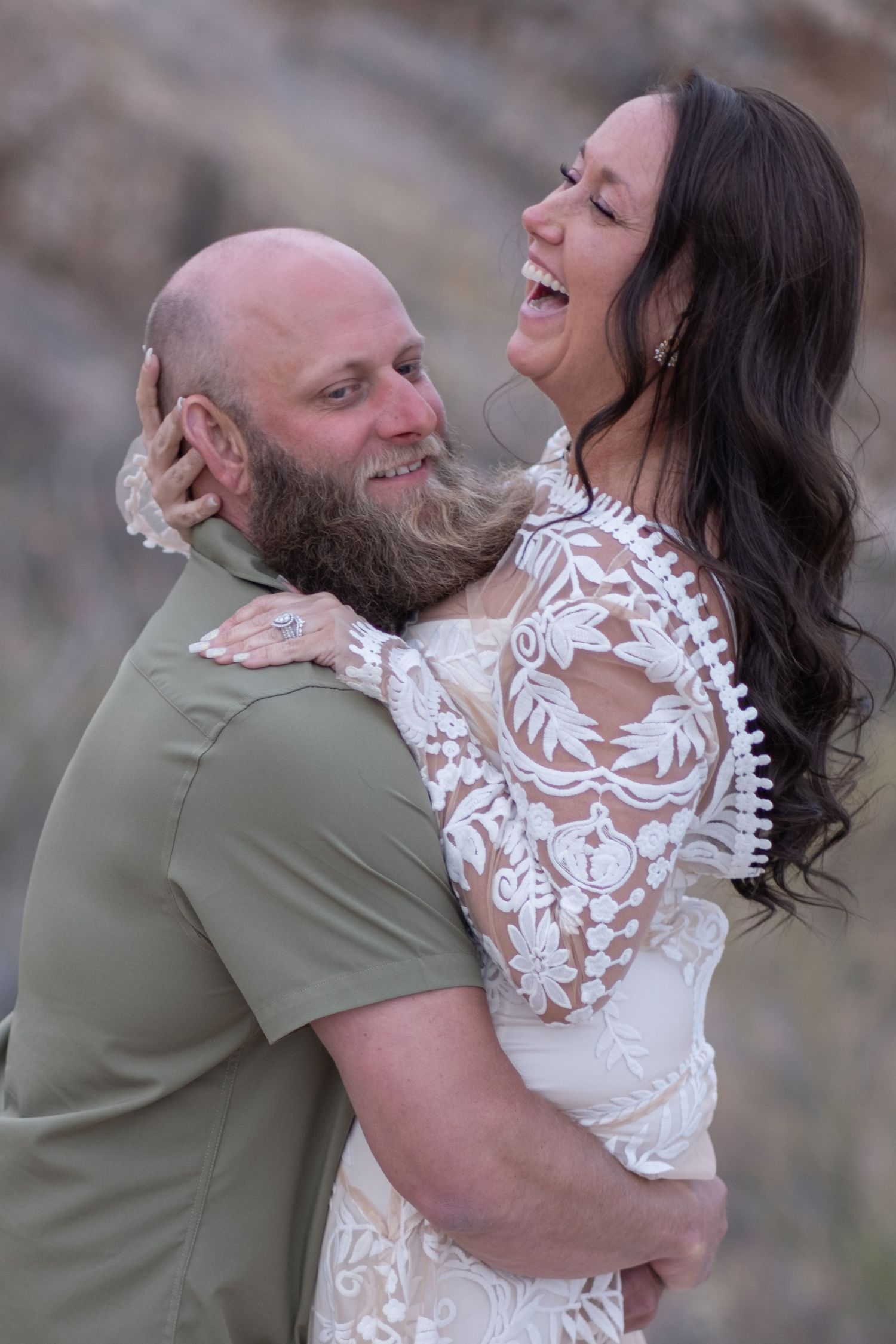 An elopement couple shares a joyful embrace and laugh together, with the bride wearing an elegant white lace dress.