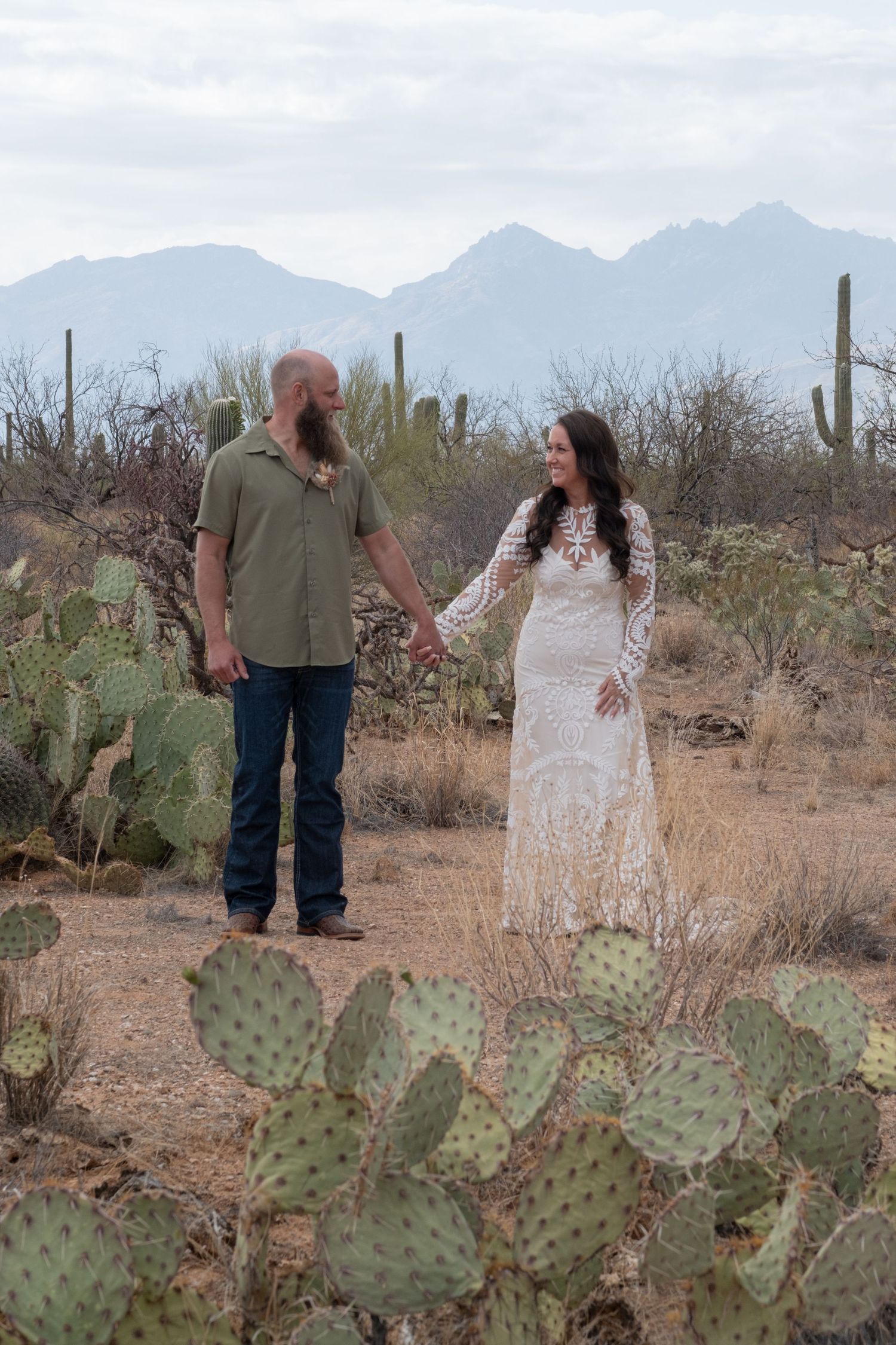 A couple shares loving moments in the desert among cacti and mountains in the background during their elopement.