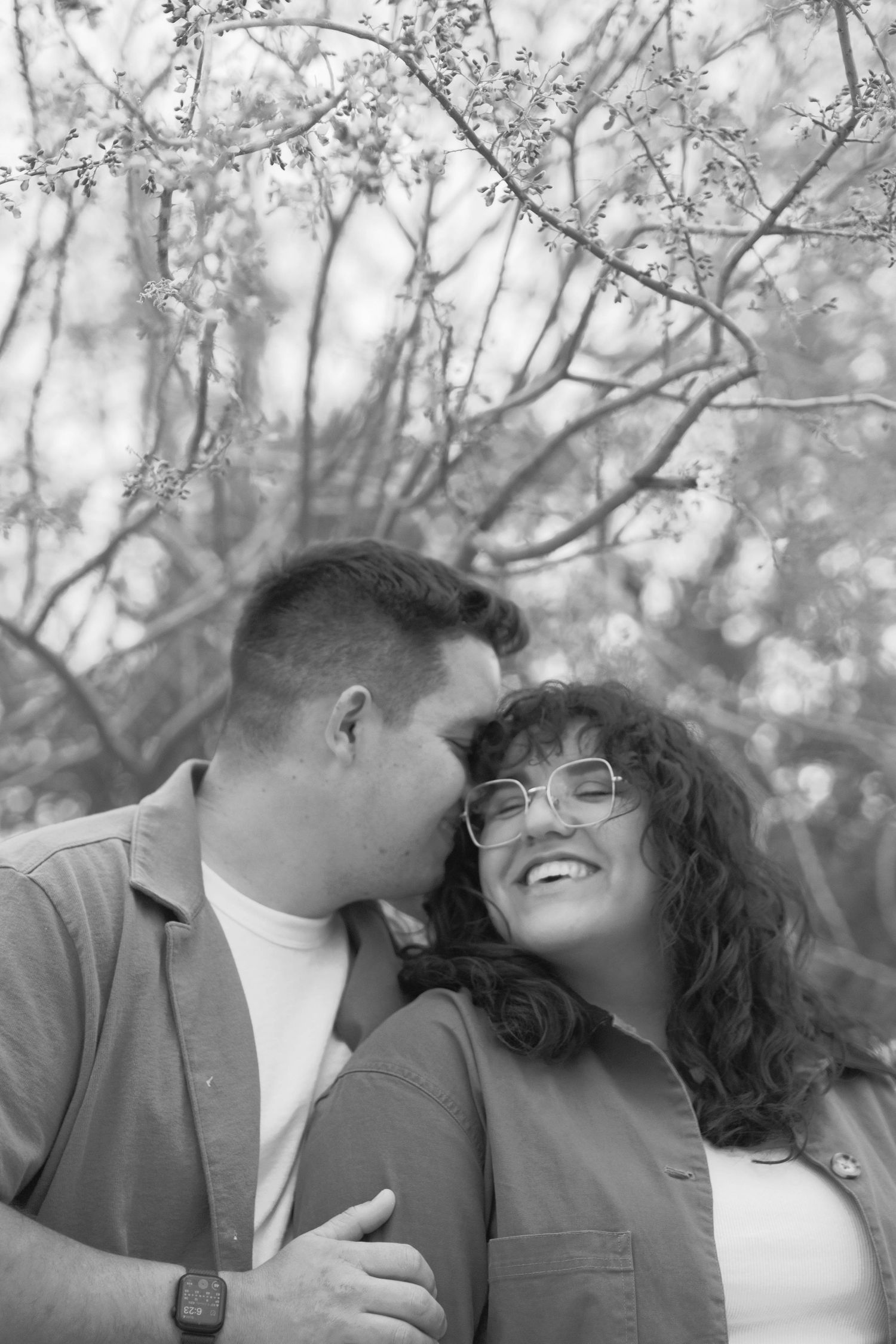 A black and white intimate portrait of a couple among blooming tree branches.