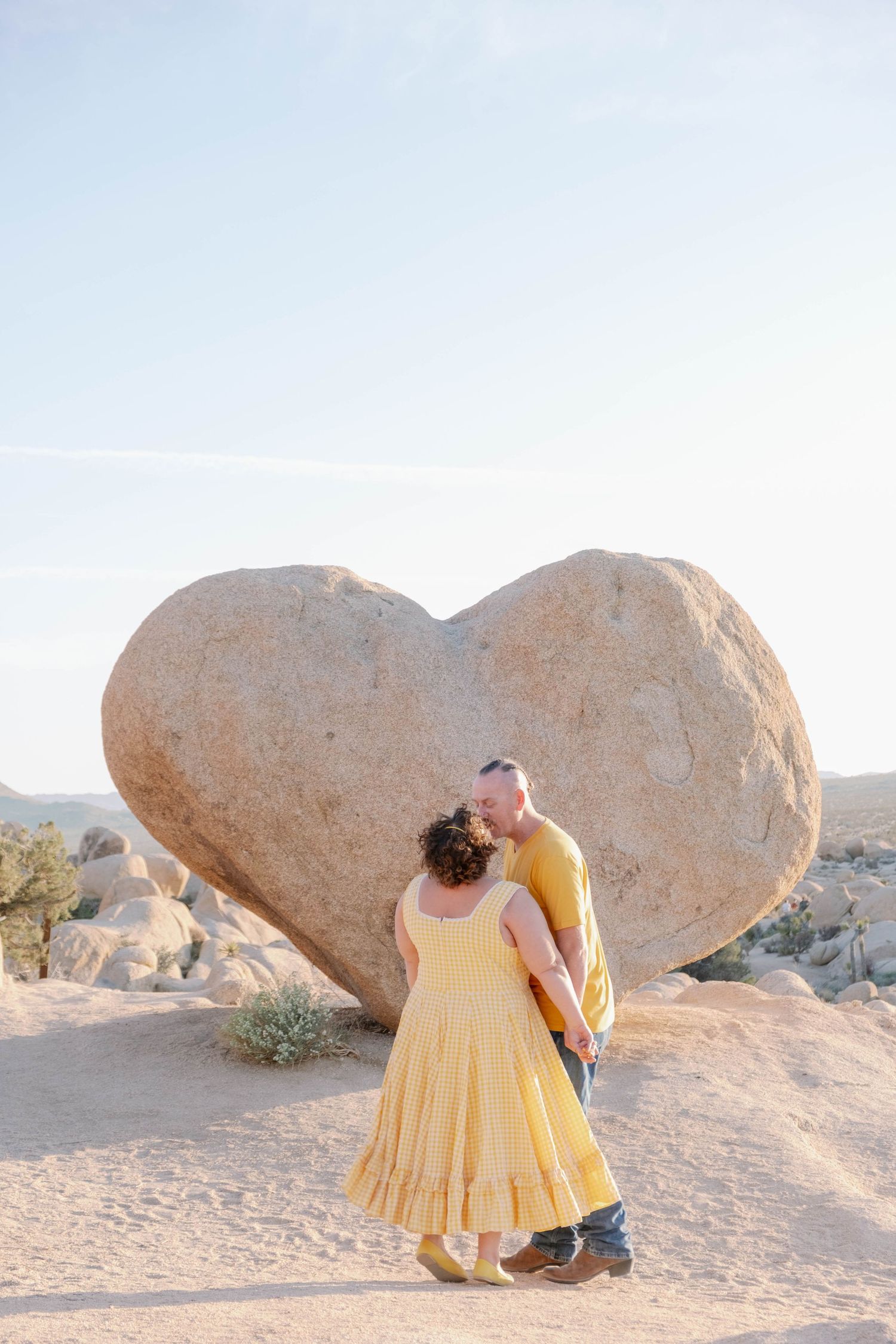 A couple poses together in front of a heart-shaped rock formation in Joshua Tree National Park.