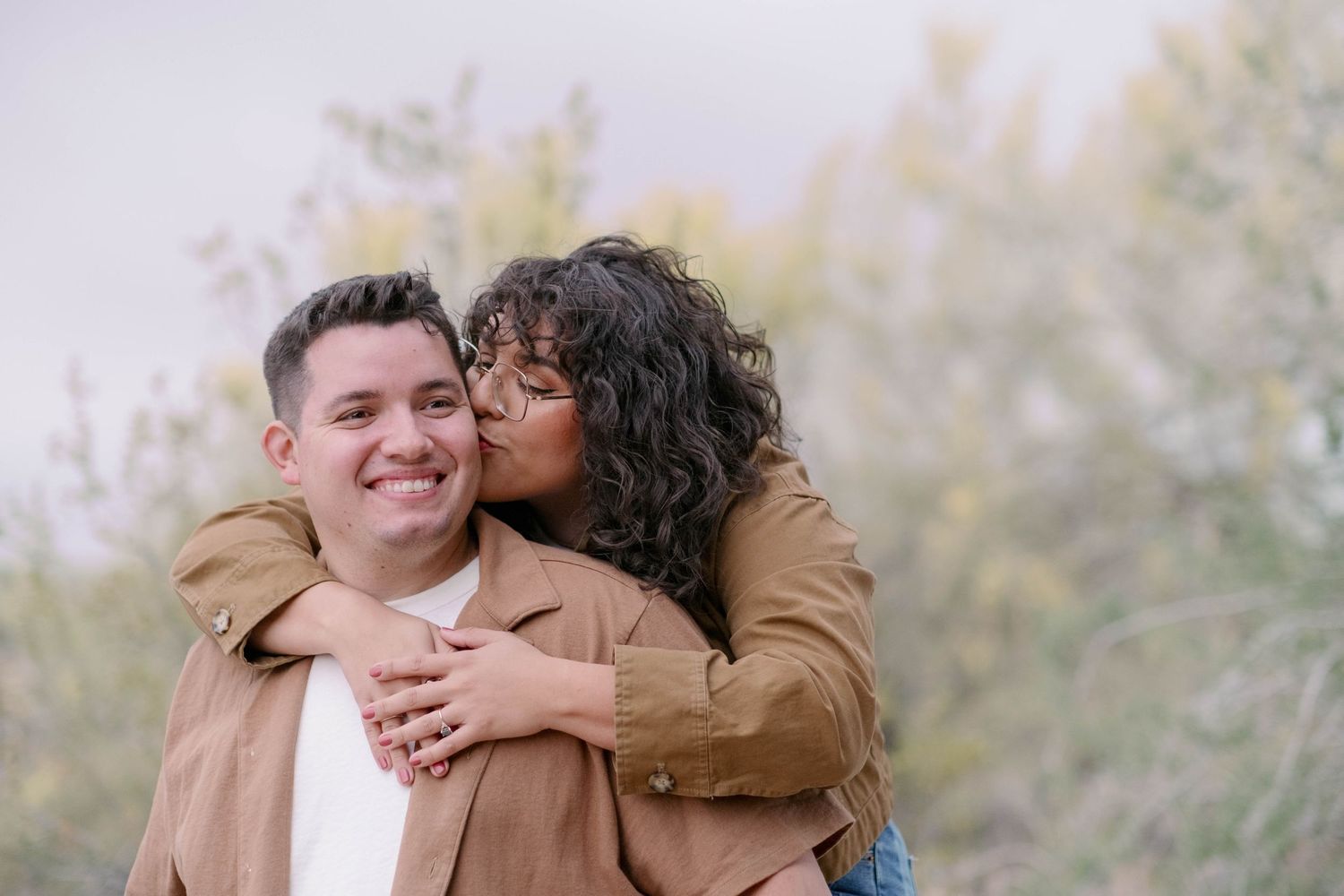 A couple shares an intimate embrace outdoors with warm lighting and natural scenery in the background.