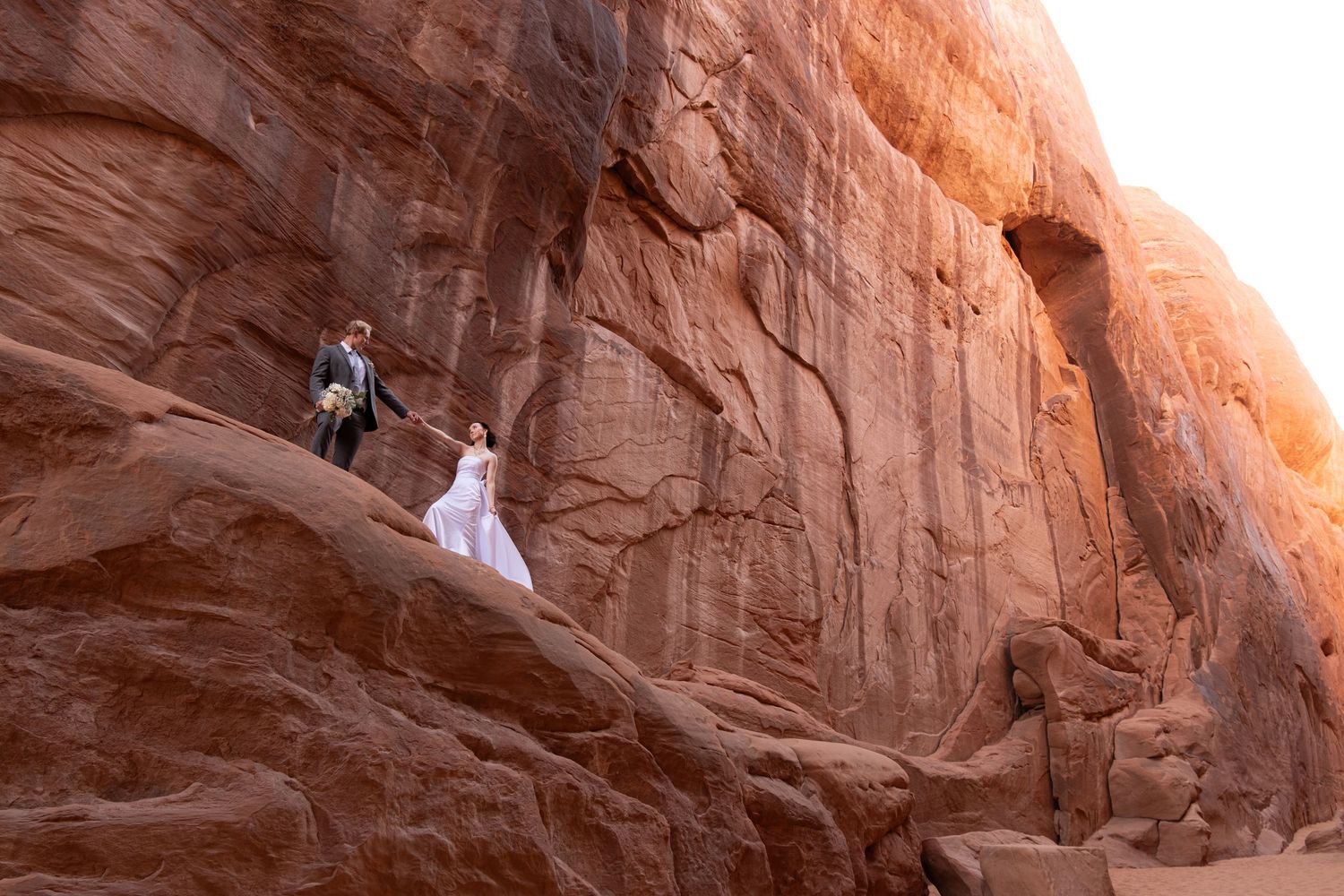 Rock climbers ascend steep red sandstone cliffs at sunset in a dramatic desert landscape.