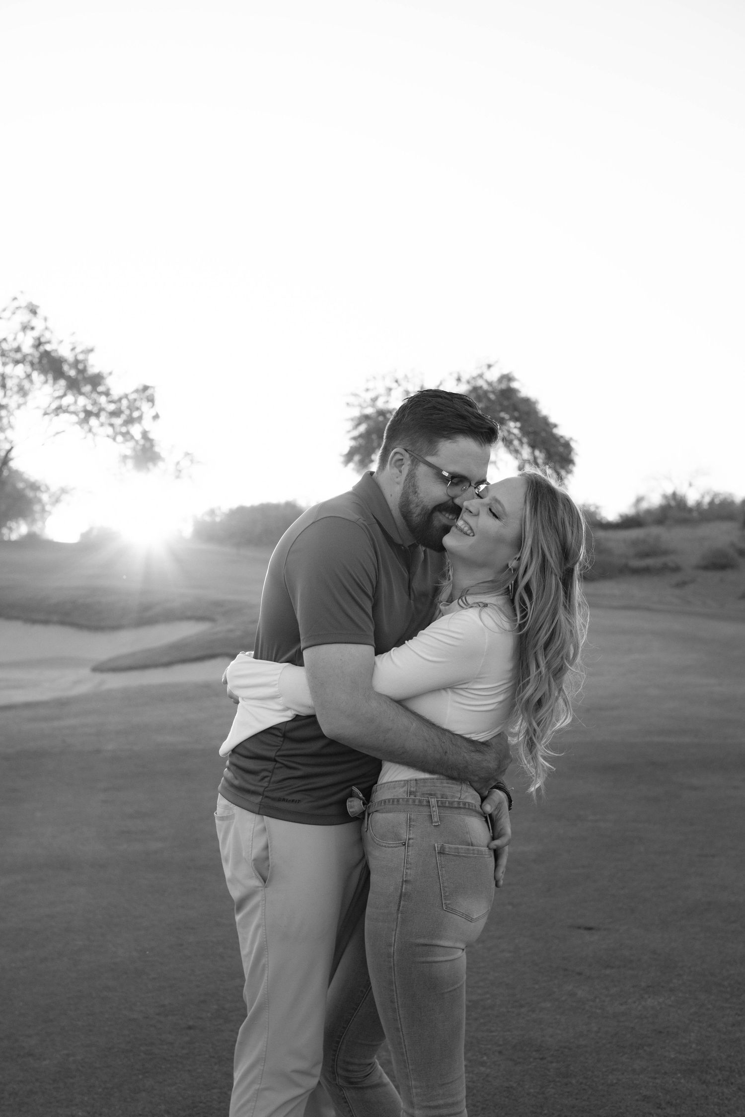 A black and white romantic moment captured on a golf course at sunset.