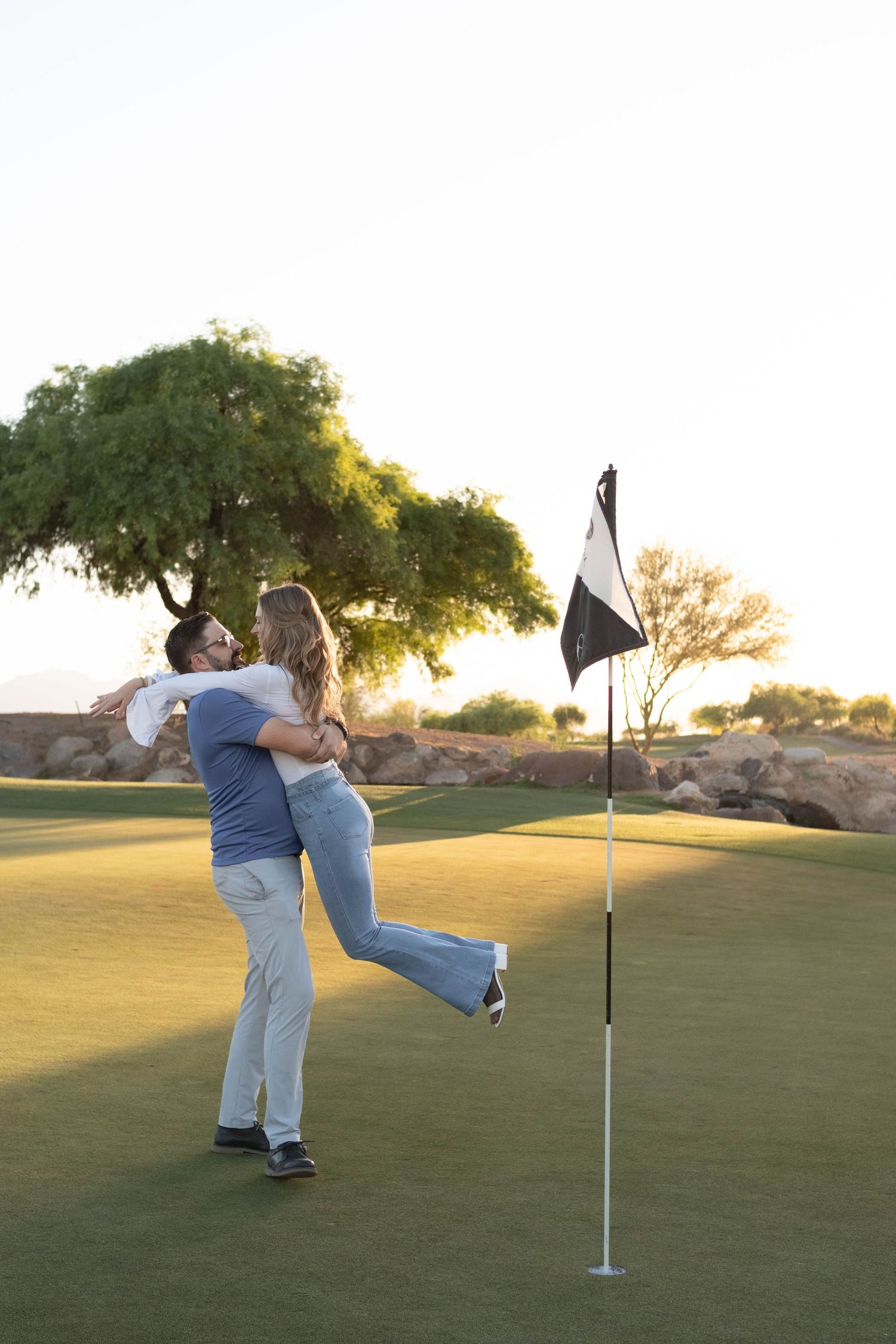 A couple shares a playful moment on a golf green during golden hour.