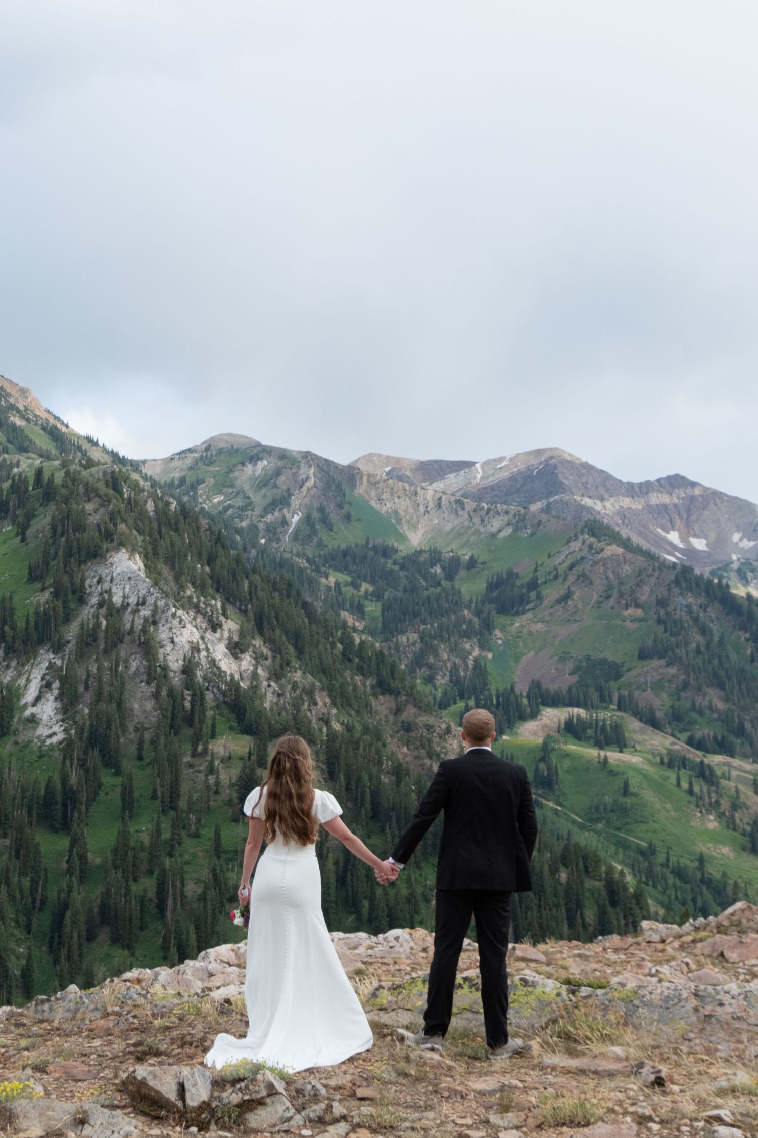 A couple taking in breathtaking mountain views while standing on a rocky overlook in an alpine setting.