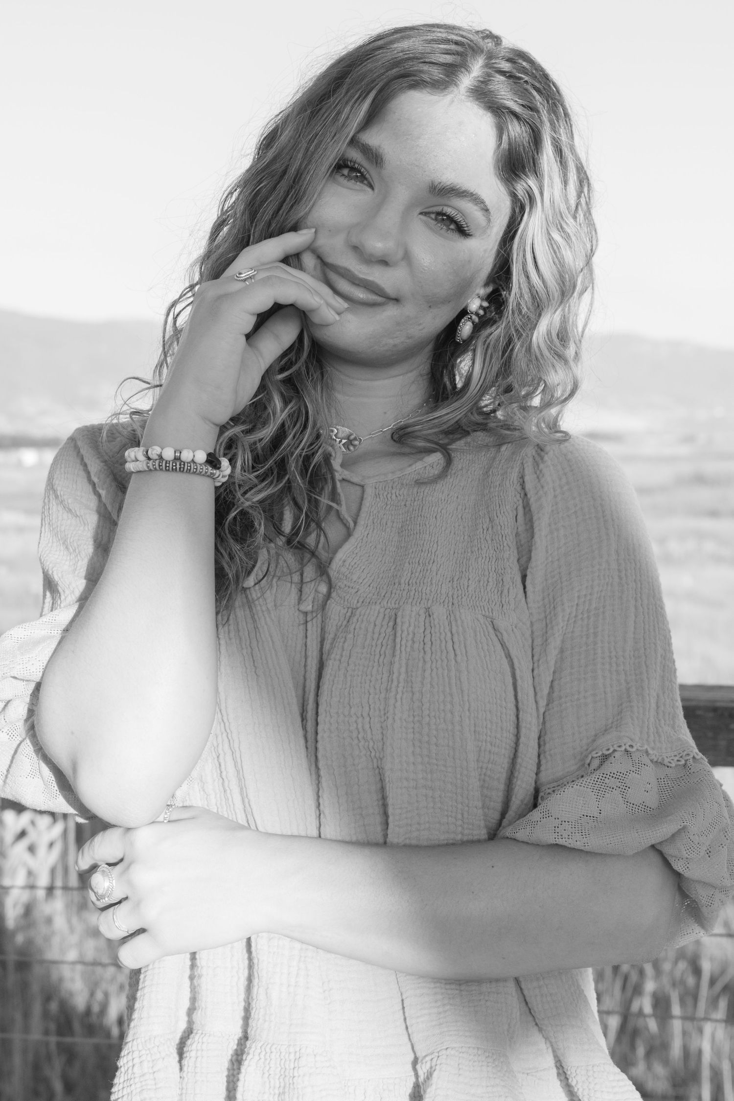 Black and white portrait of a smiling woman with curly hair wearing a casual blouse with puff sleeves outdoors.