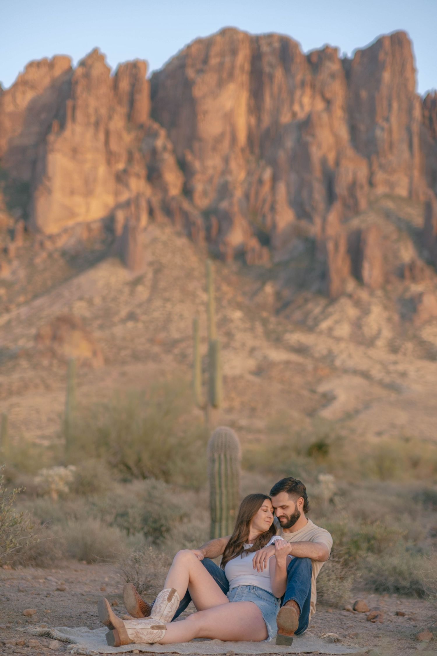 A couple shares an intimate moment while sitting in the desert with majestic mountain peaks behind them.