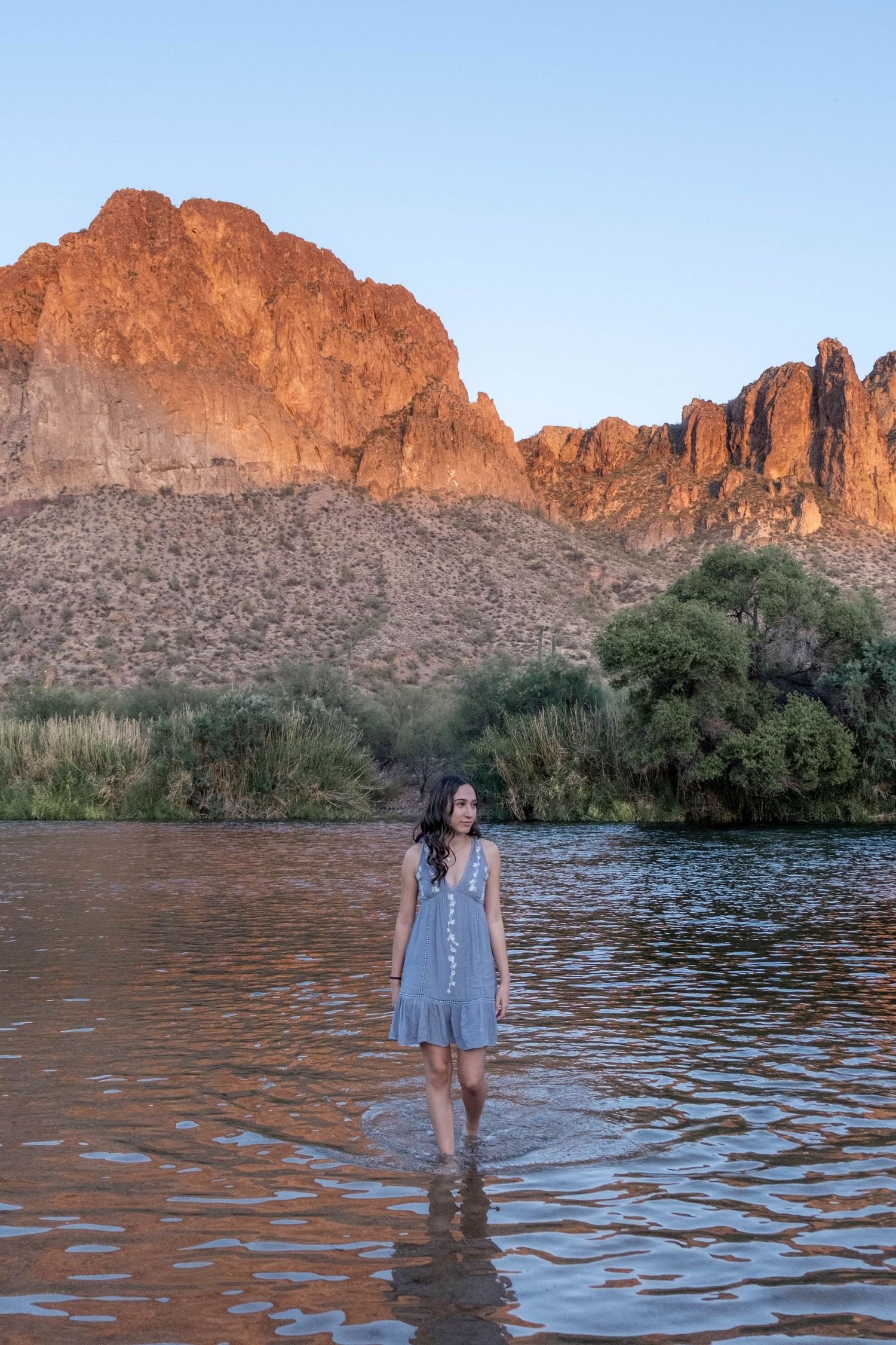 Someone wades in golden-lit water against a backdrop of dramatic desert cliffs.