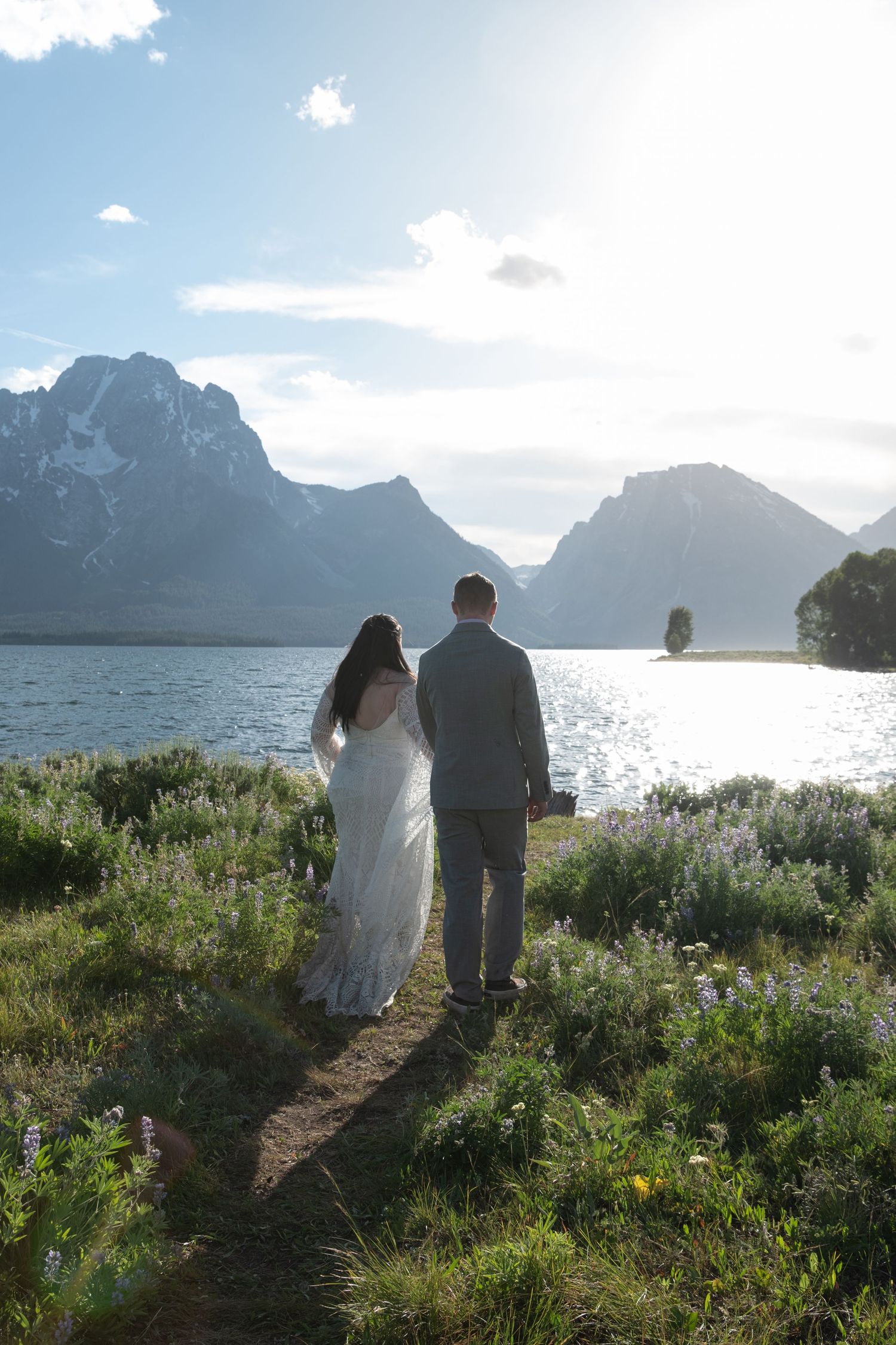 A couple walks along a scenic mountain path by Jackson Lake in Grand Teton National Park at sunset.