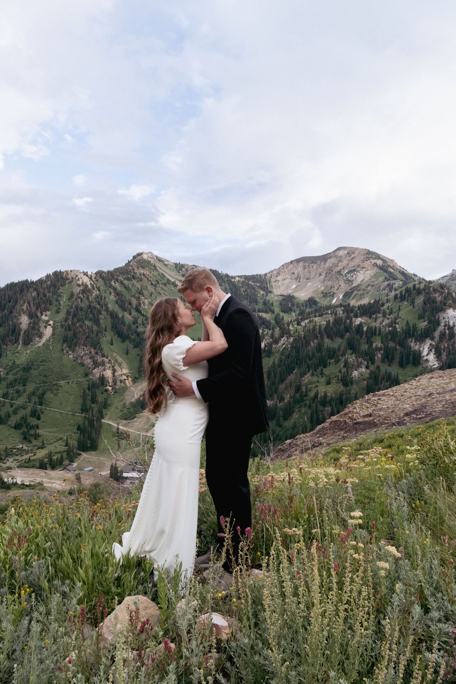 A romantic wedding couple embraces in a scenic mountain meadow surrounded by wildflowers at Alta, Utah.