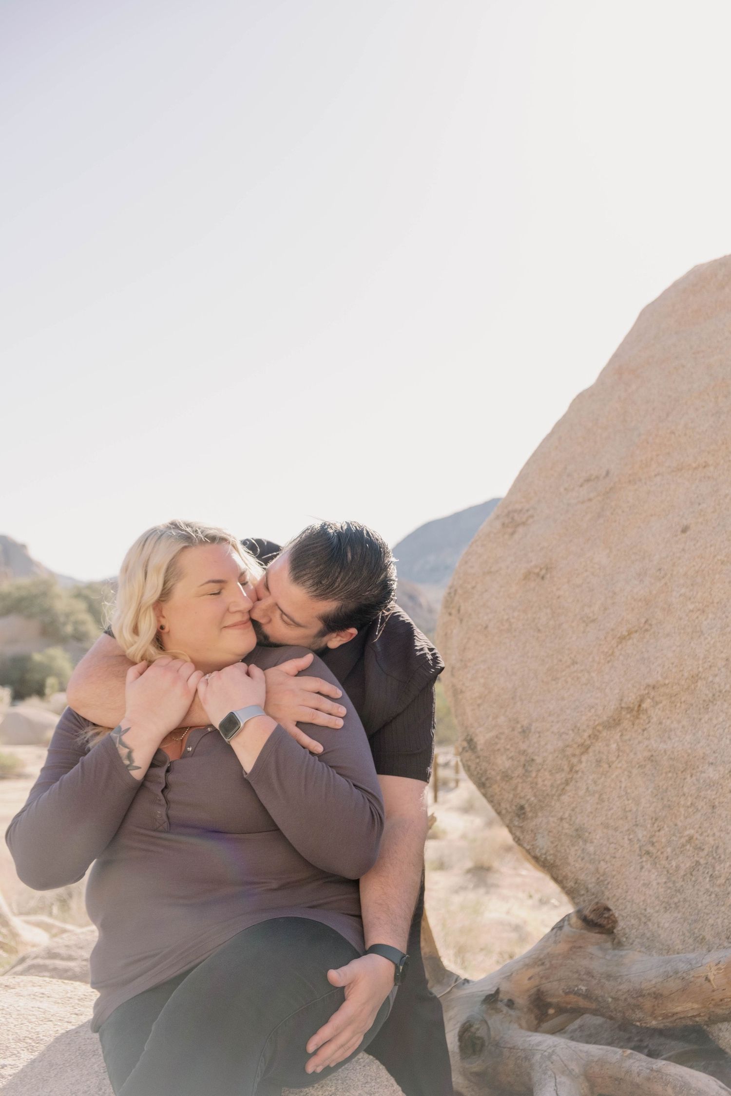 A couple shares an intimate embrace while sitting on desert rocks.