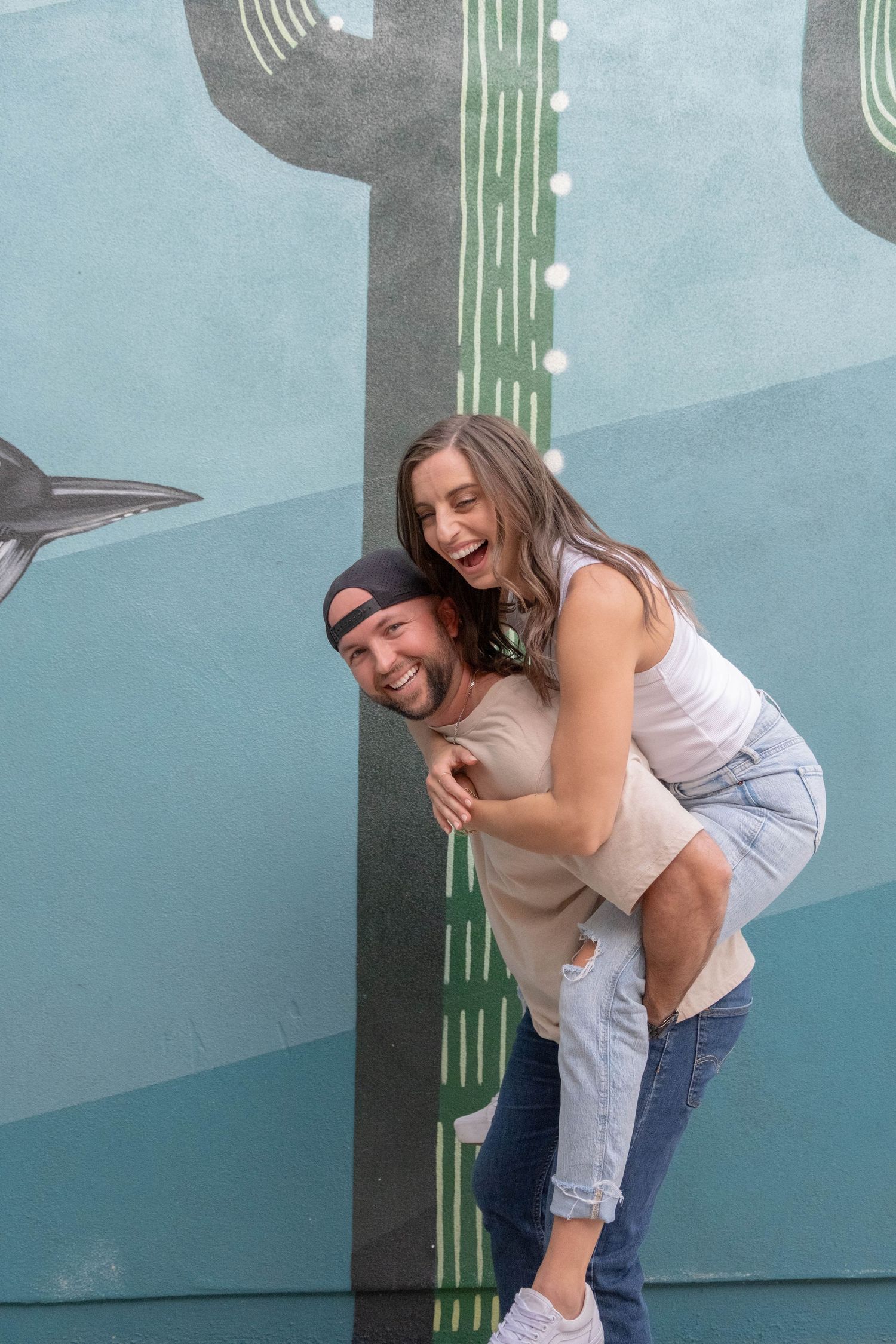 Adventurous couple laughing together piggybacking the other through downtown Chandler, Arizona.
