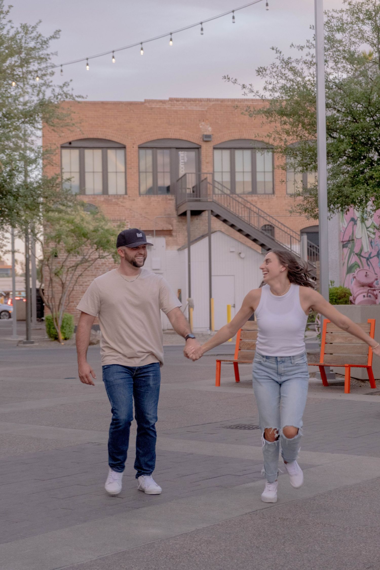 Couple dancing and having fun in an outdoor plaza with string lights.