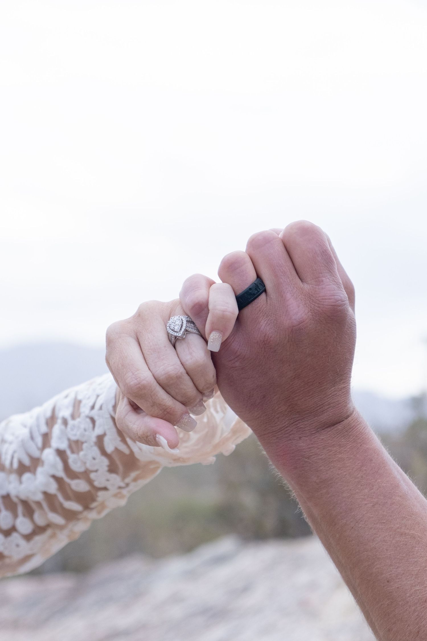 Close-up view of two hands touching with one wearing a lace sleeve and a ring in a romantic gesture during their elopement.