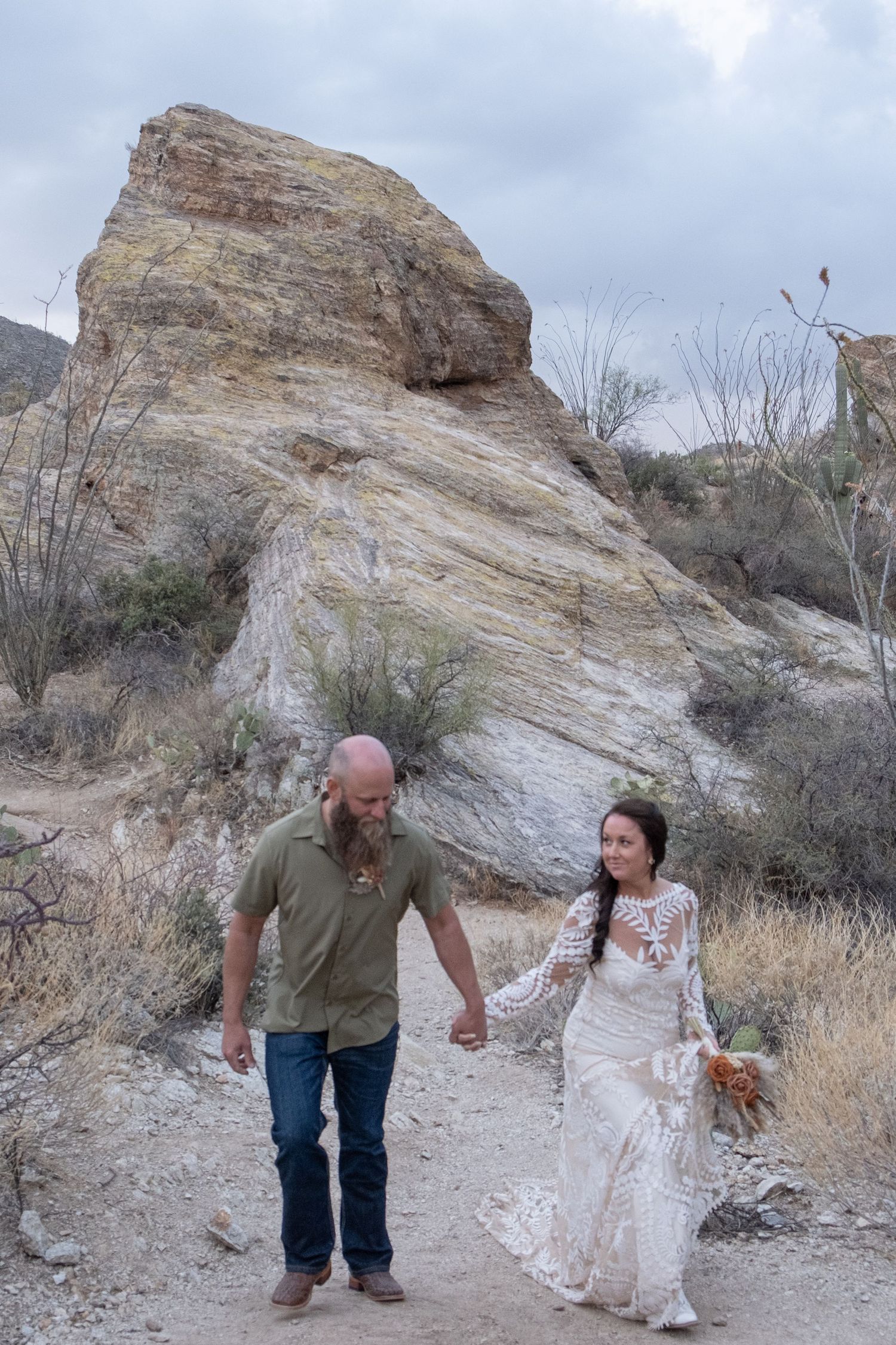 A newly married couple interact outdoors against a dramatic rocky desert backdrop on a cloudy day during their elopement.