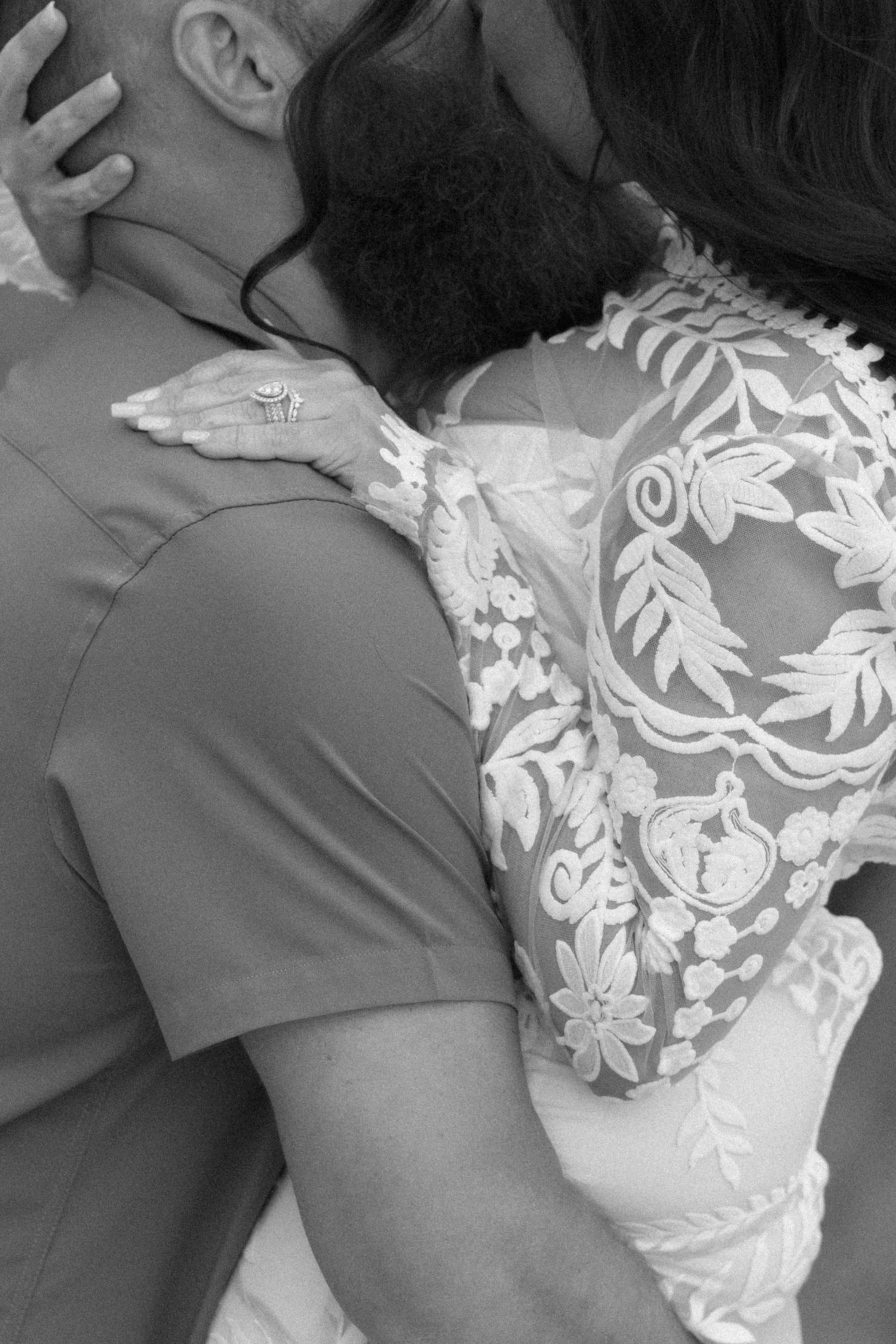 Elopement detail of white floral lace pattern on sheer bridal gown fabric shown in black and white photograph.