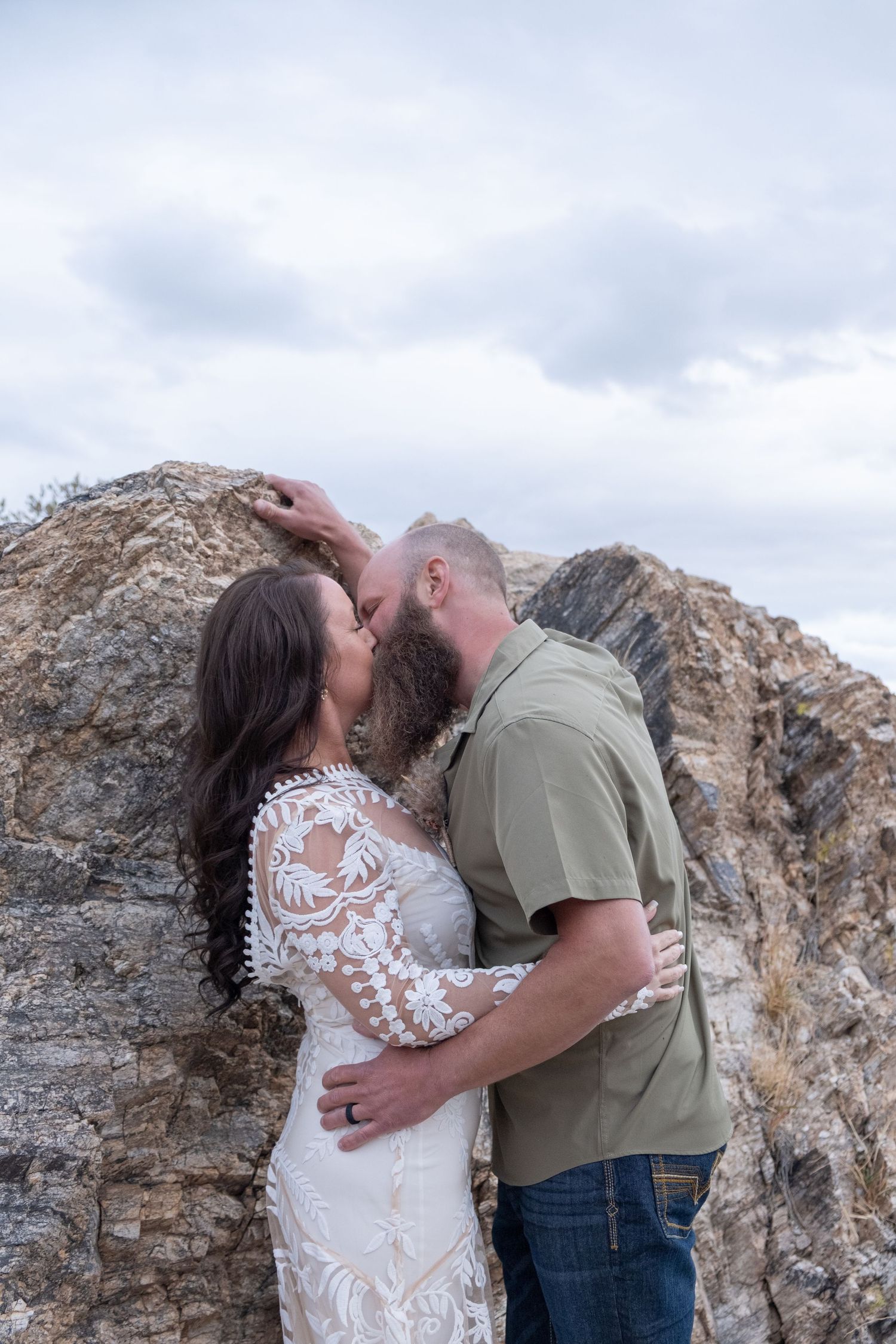 Couple embraces and kisses against rocky mountain backdrop with cloudy sky during their elopement.