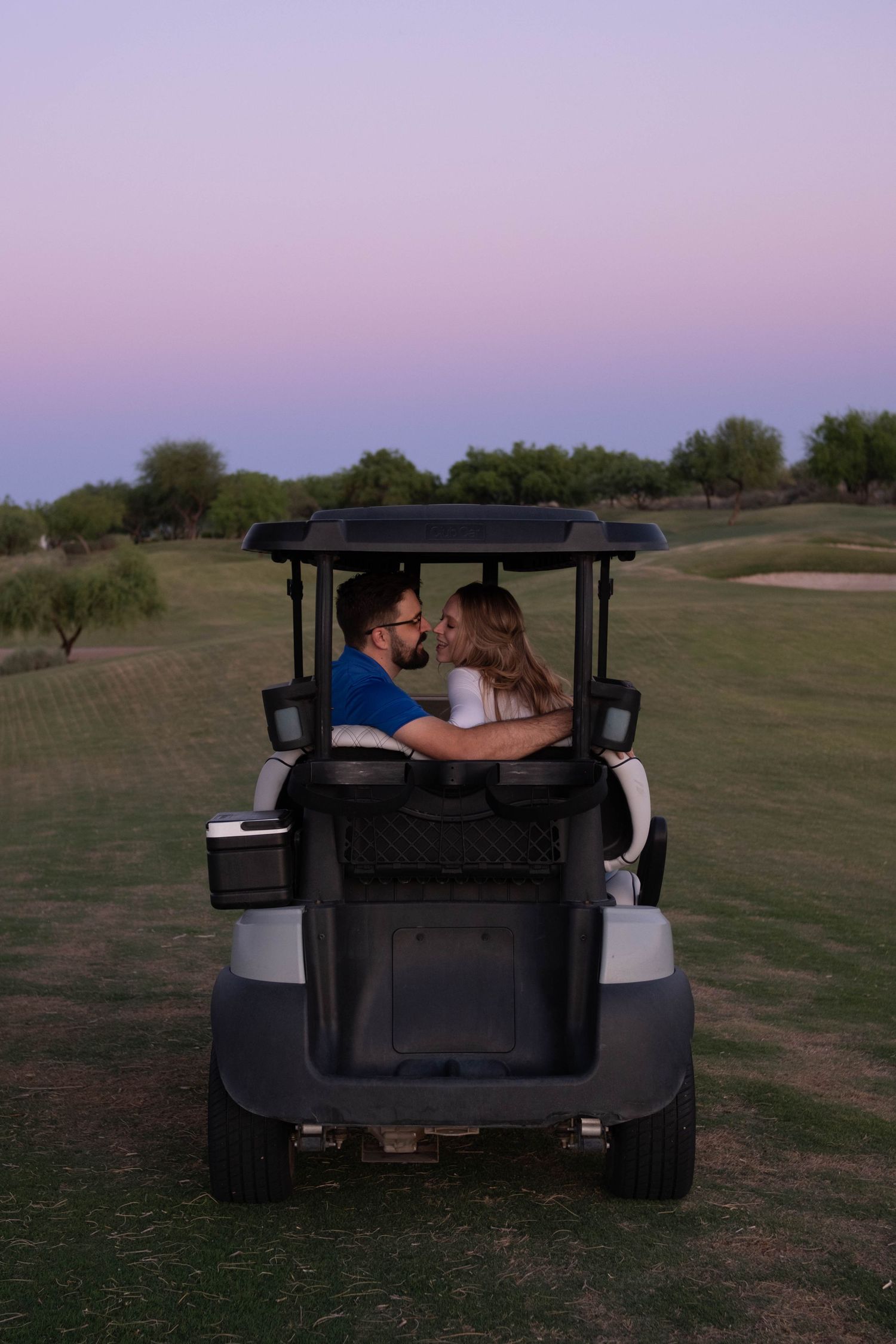 A couple sharing an intimate moment in a golf cart during twilight.