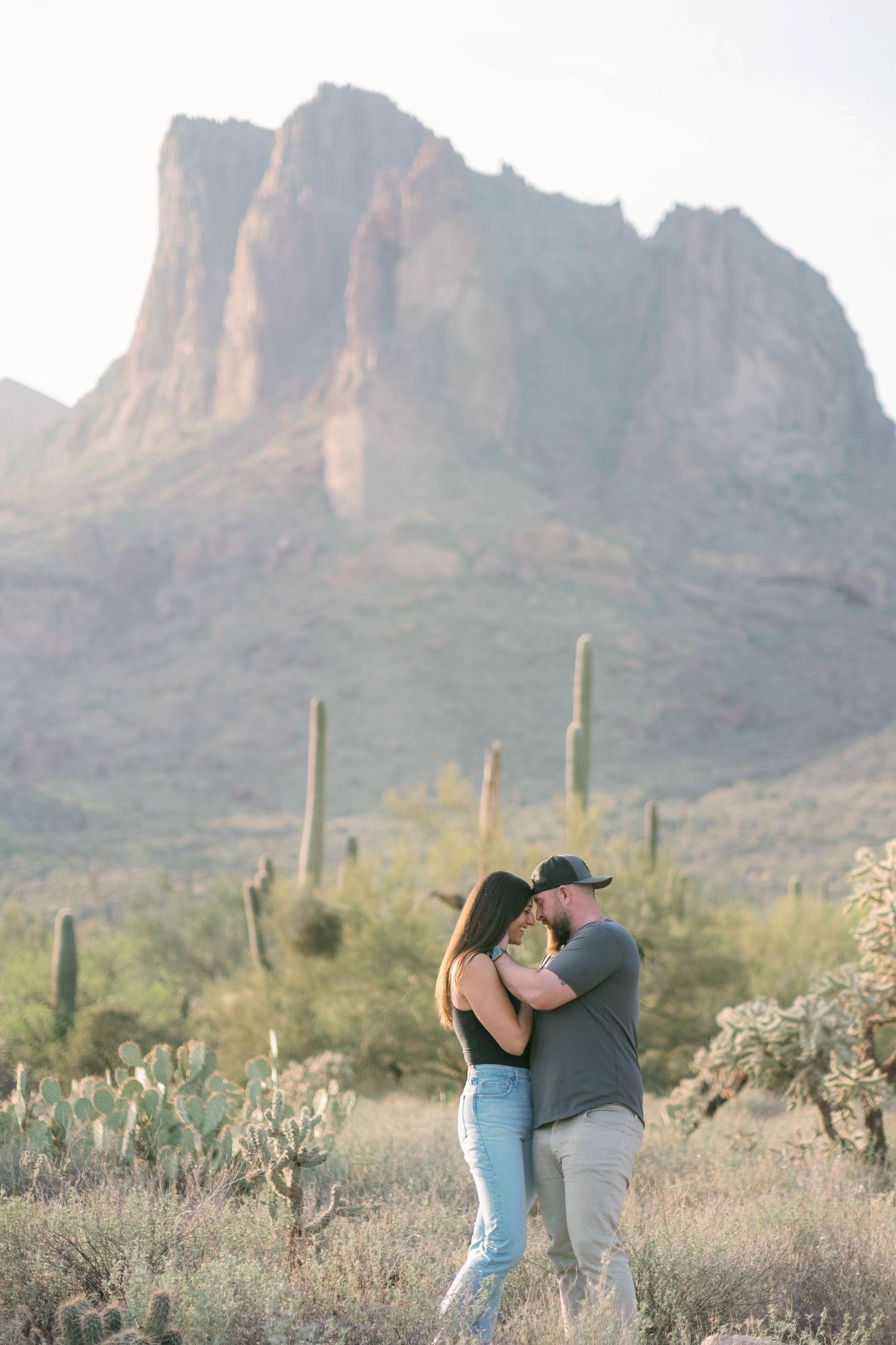 Couple embracing in desert setting with saguaro cacti and mountain backdrop.