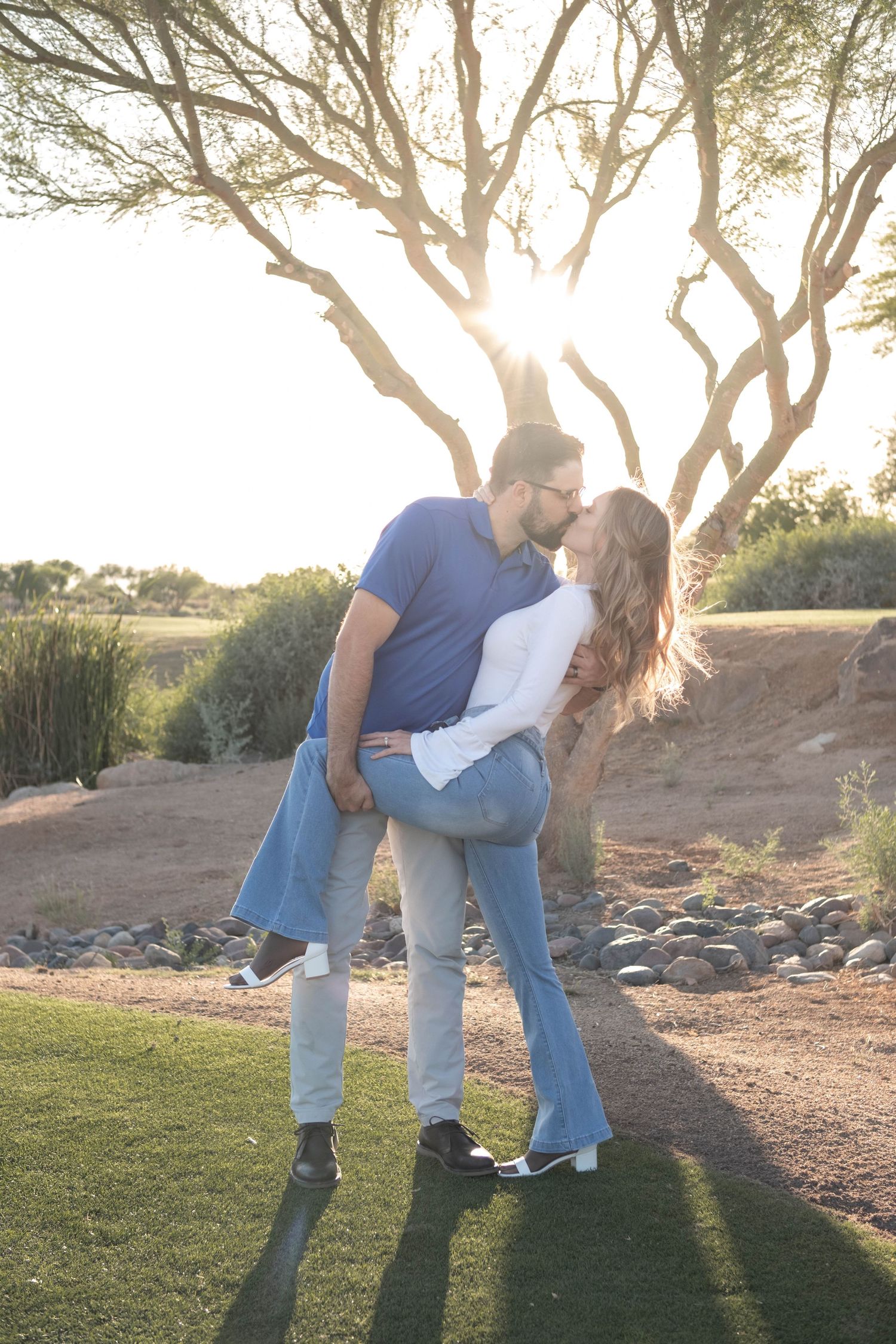 A romantic sunset embrace between a couple under a tree on a golf course.