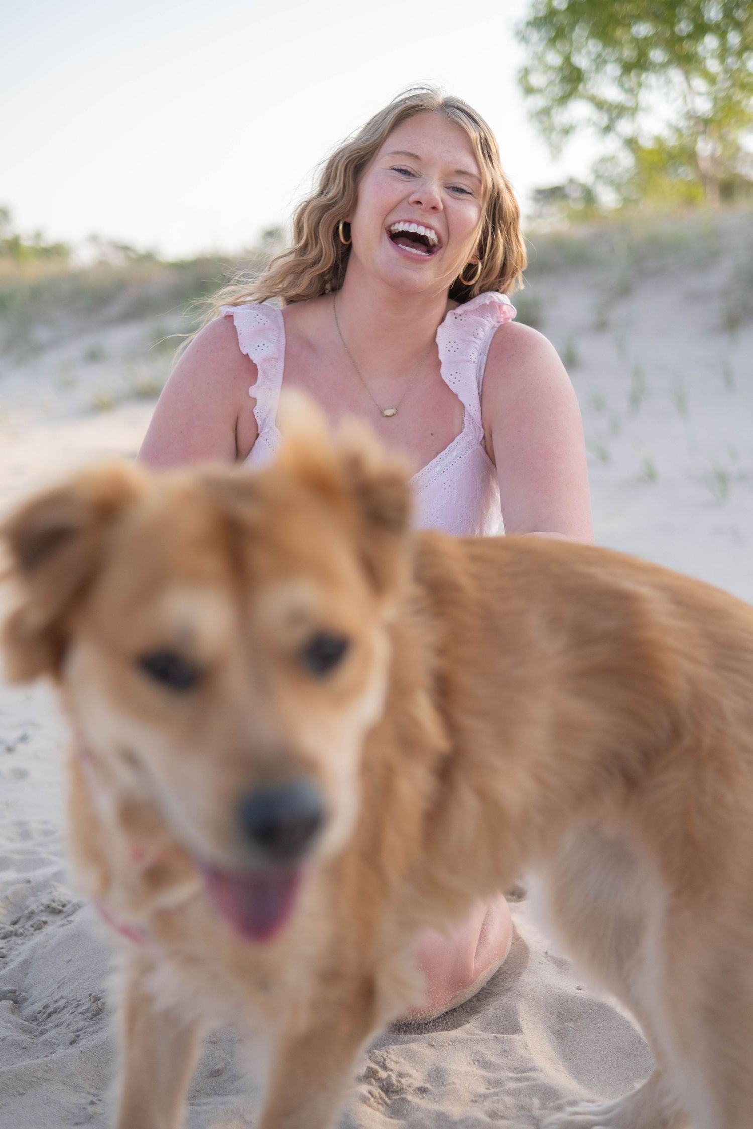 A happy moment captured at the beach with a playful golden-brown dog in the foreground on sandy terrain.