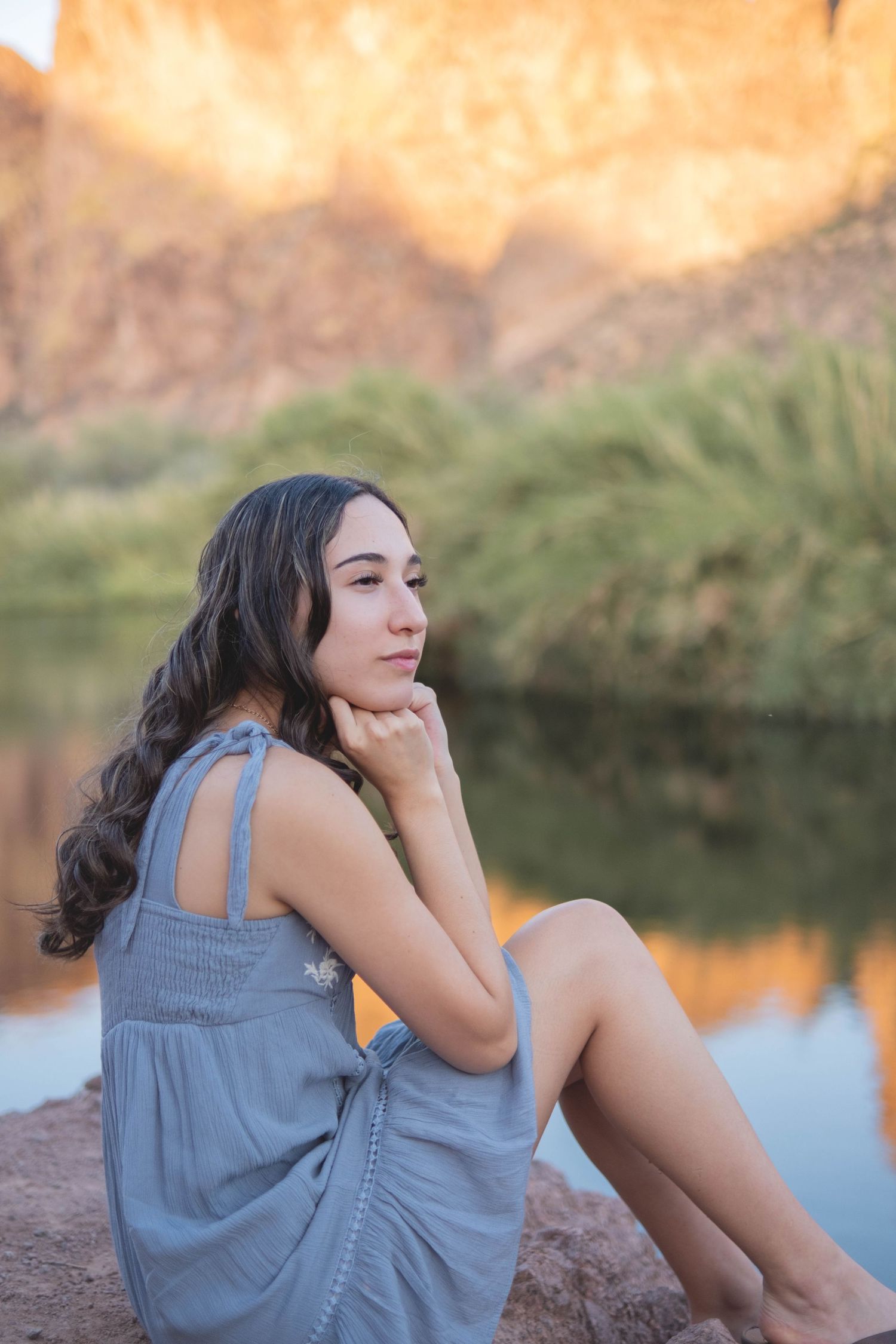 Portrait session of young woman sitting thoughtfully by a desert lake during golden hour.