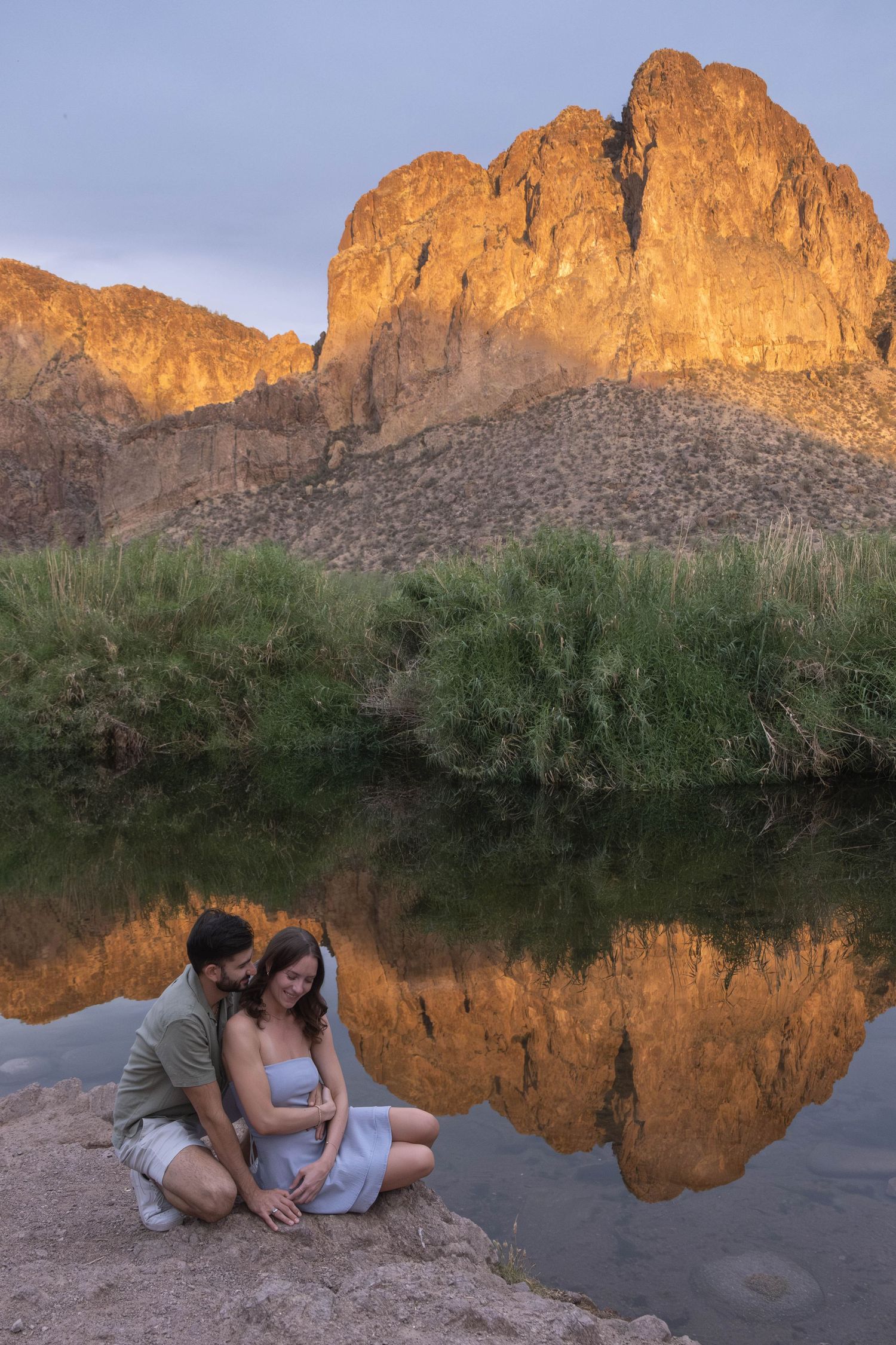 A romantic photo session by a scenic desert lake with mountains reflecting in calm waters.