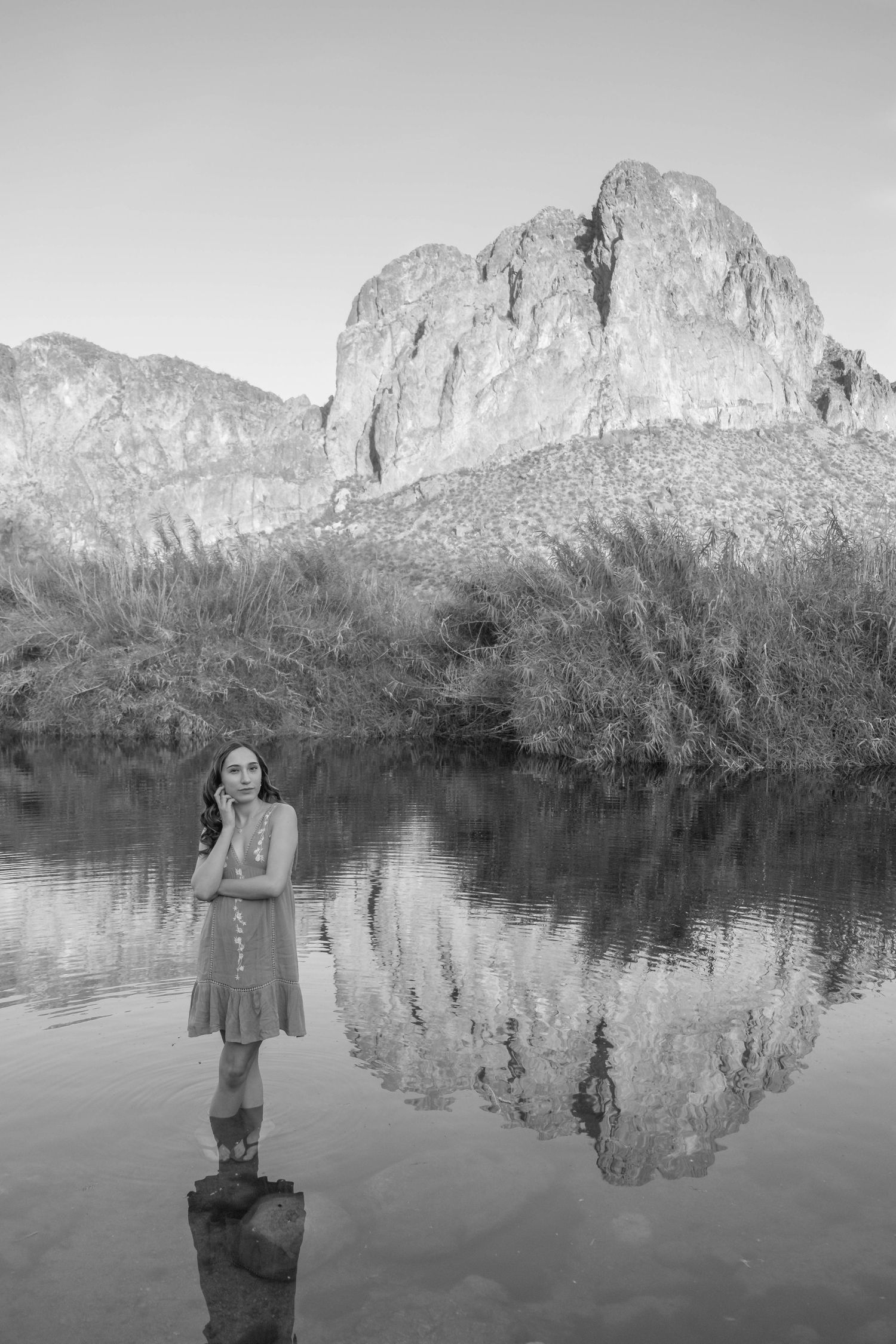 Black and white photo of a figure standing in still water with mountain reflections.