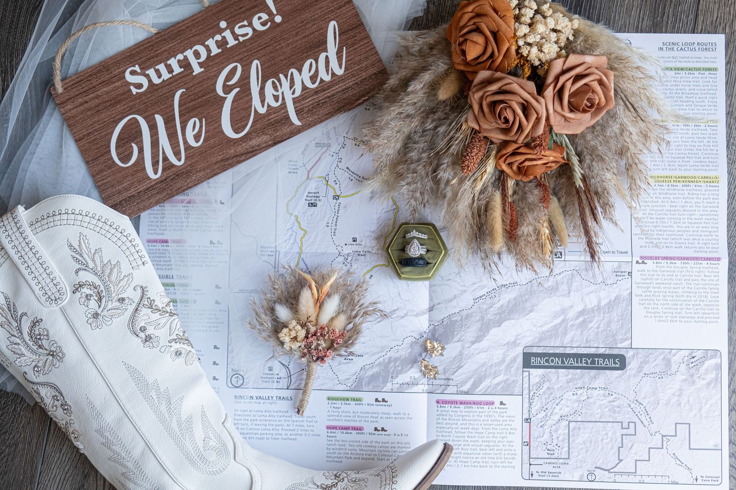 A collection of elegant wedding invitations with dried flowers and wooden signs arranged on white paper surfaces for an elopement.