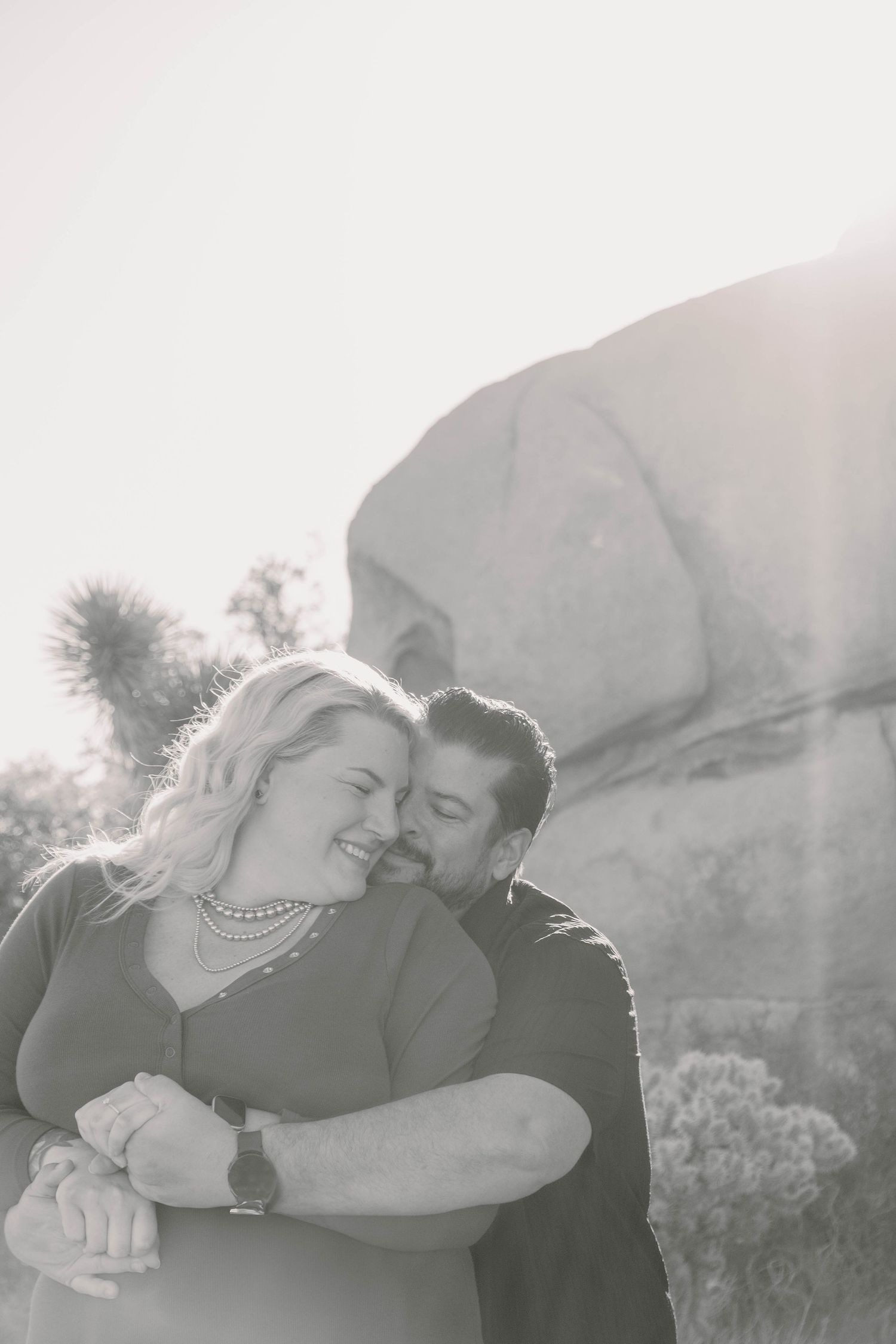 A black and white portrait of a couple sharing a tender moment outdoors.