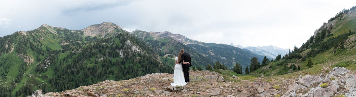 Panoramic mountain landscape with rugged peaks and alpine meadows stretches across the horizon on a cloudy day.