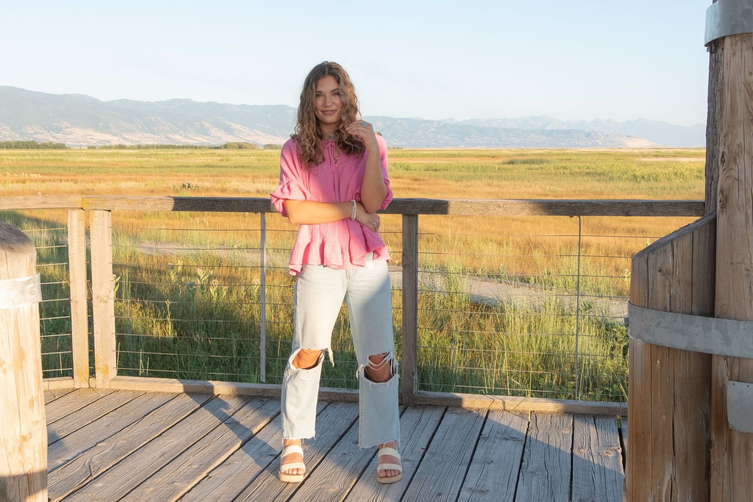 People relaxing and enjoying sunset views from a wooden boardwalk overlooking scenic mountains and grasslands.