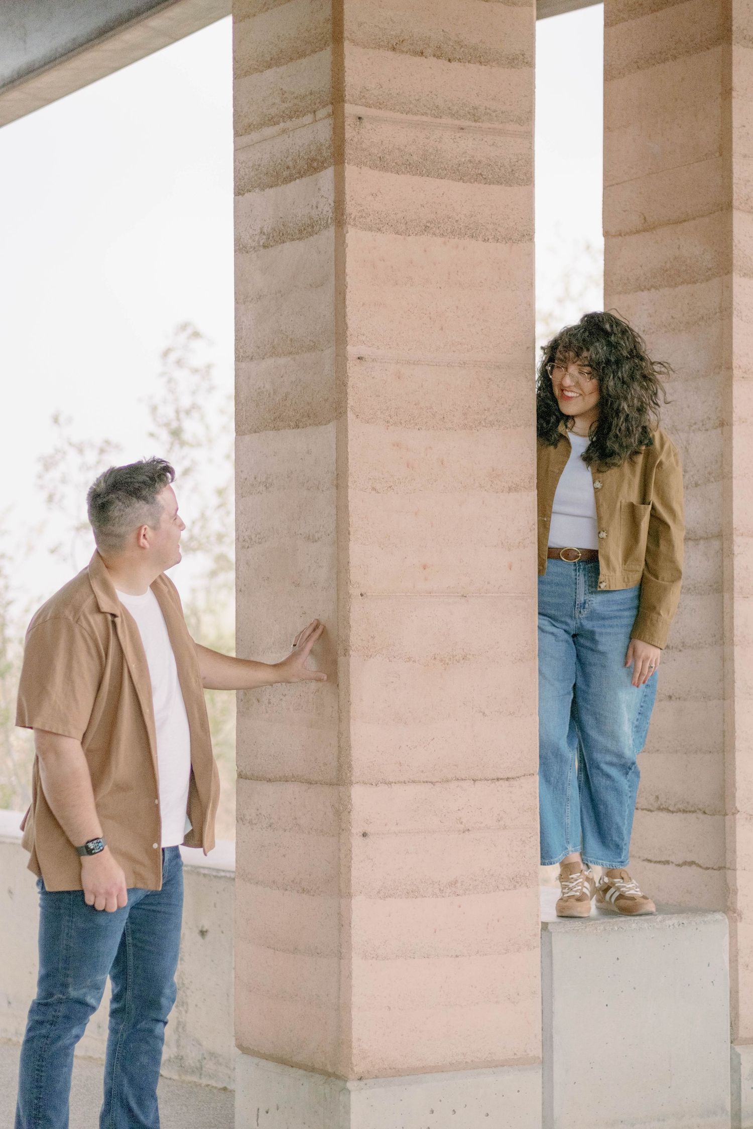 Two people pose playfully in a modern concrete structure with natural lighting.